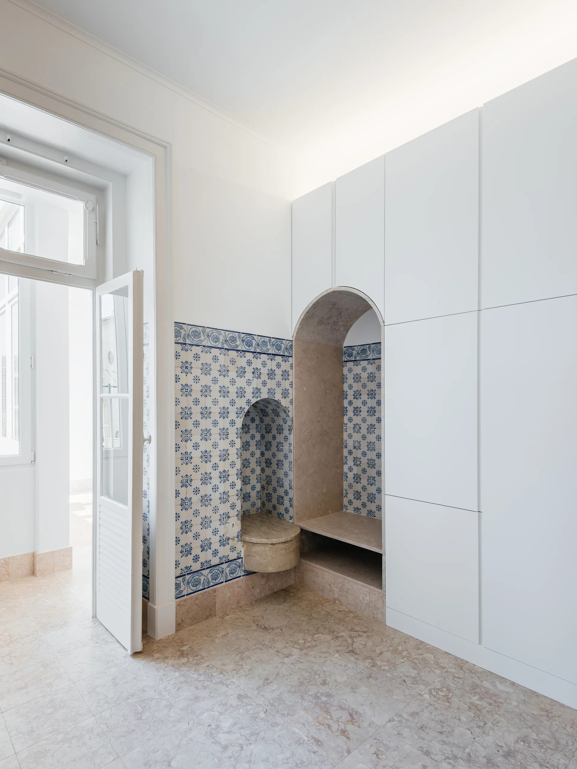 Modern white floor to ceiling cabinets feature an integrated pink marble archway alongside traditional blue and white patterned tile wall niches.