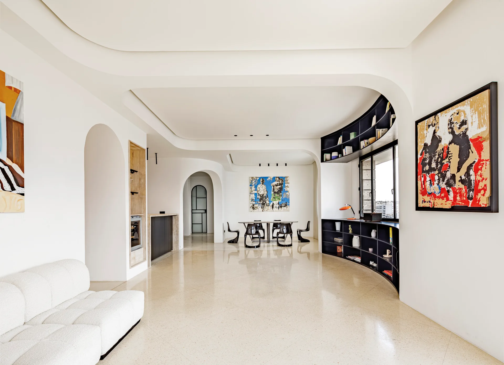 A minimalist open-plan interior with polished light stone floors, arched doorways, a white sofa, and a custom curved black shelving unit.
