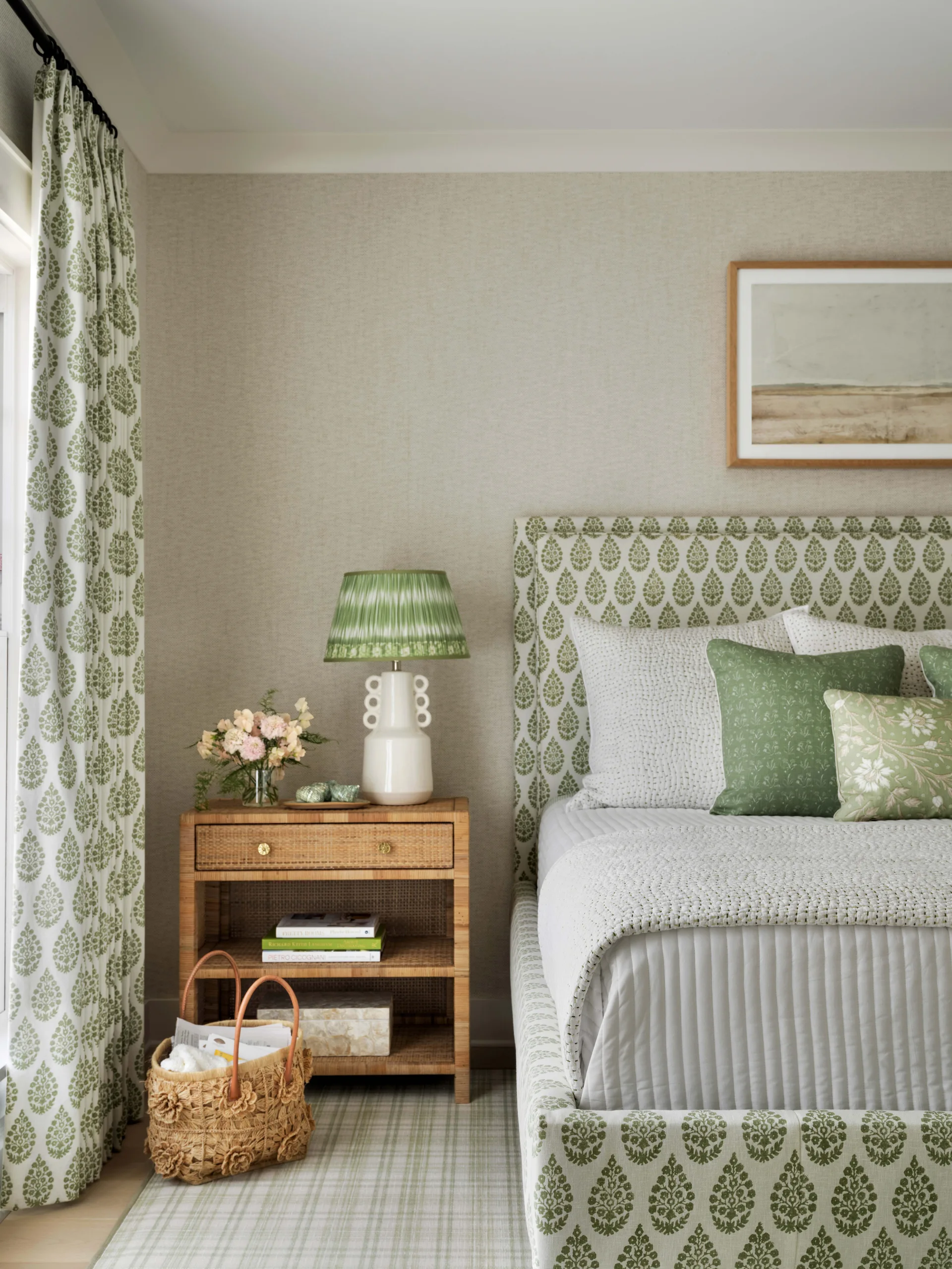 A bright cottage bedroom featuring an upholstered bed and curtains in matching sage green botanical print fabric next to a rattan nightstand.