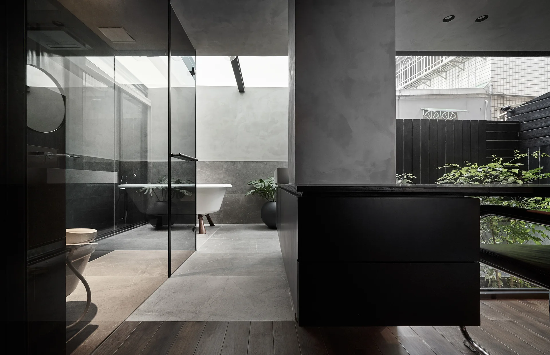 A modern gray bathroom features a glass partition separating a wet area with a freestanding white bathtub under a skylight next to a black vanity.