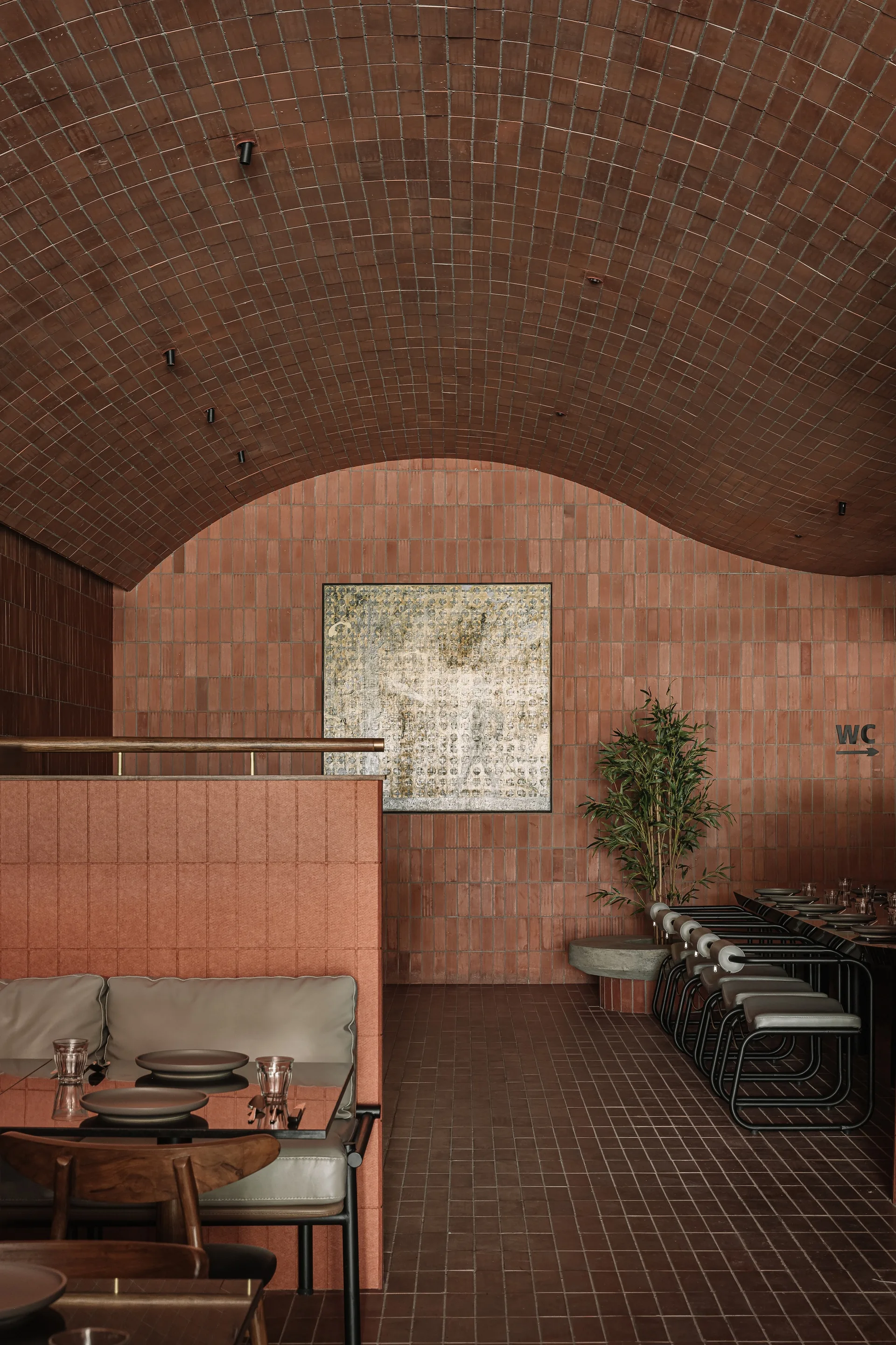 A dining room features tables and booths beneath a barrel-vaulted ceiling and walls covered in small vertical terracotta tiles.