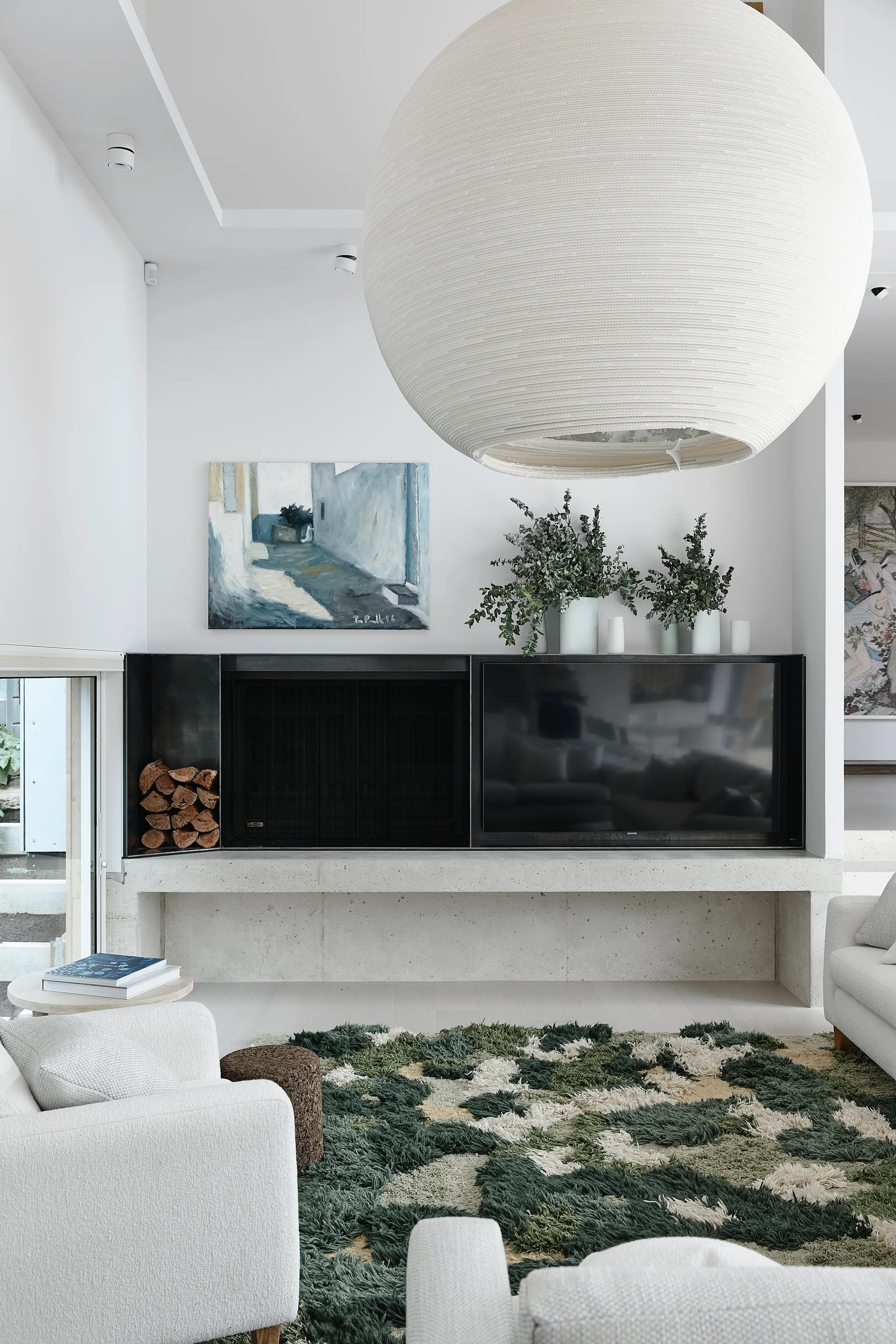 A contemporary living room featuring a massive white sphere pendant light, a low concrete-like fireplace hearth, and a textured green and white shag rug.