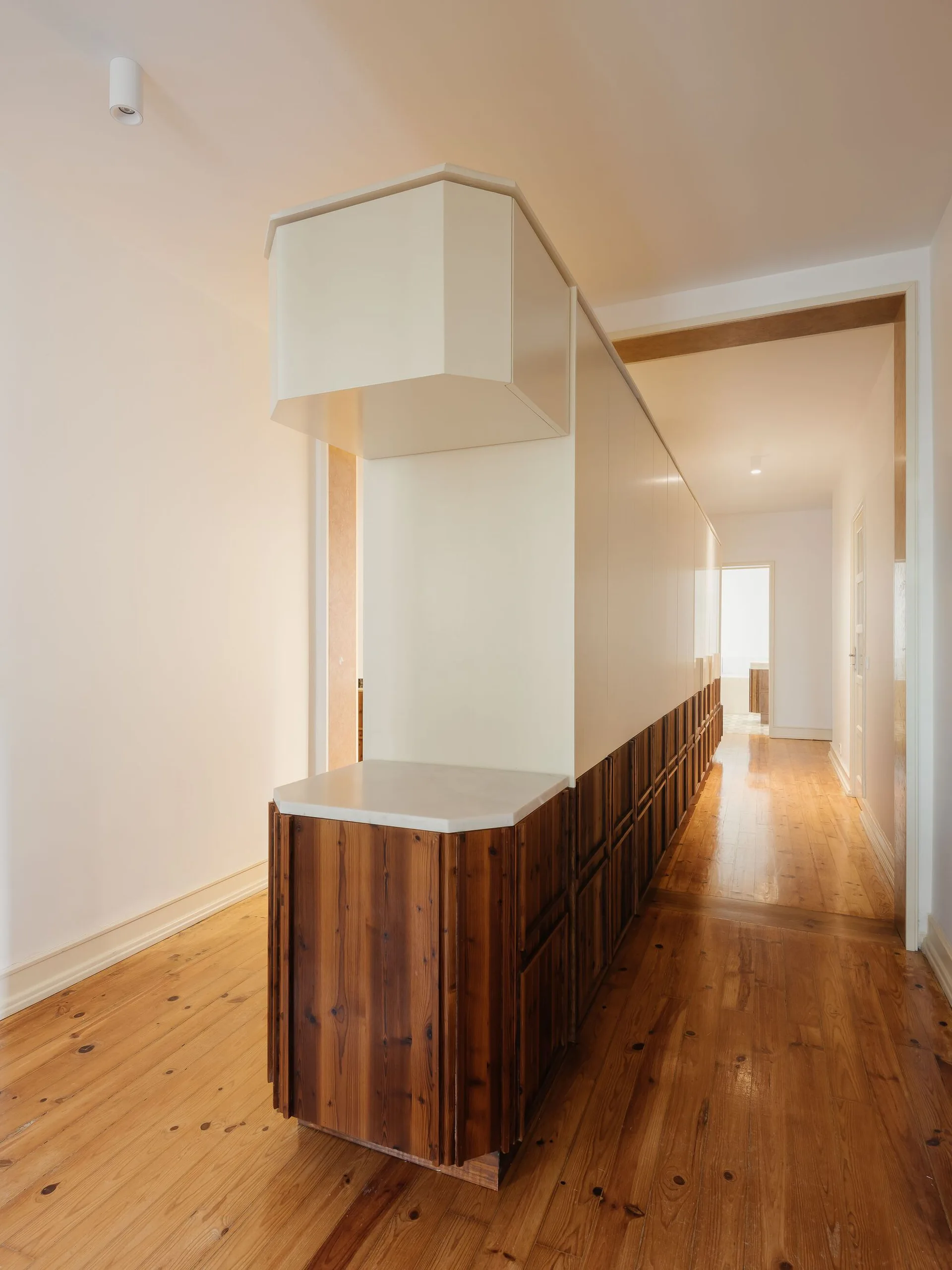 A bright hallway featuring hardwood floors and a long custom built-in cabinet with white upper panels and natural wood lower drawers.