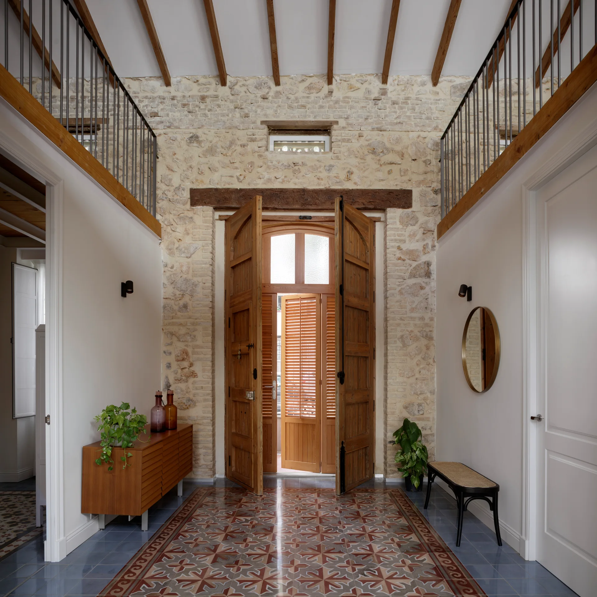 A rustic entryway featuring exposed stone masonry walls, a large wooden double door, and patterned tile flooring bordered by solid blue tiles.