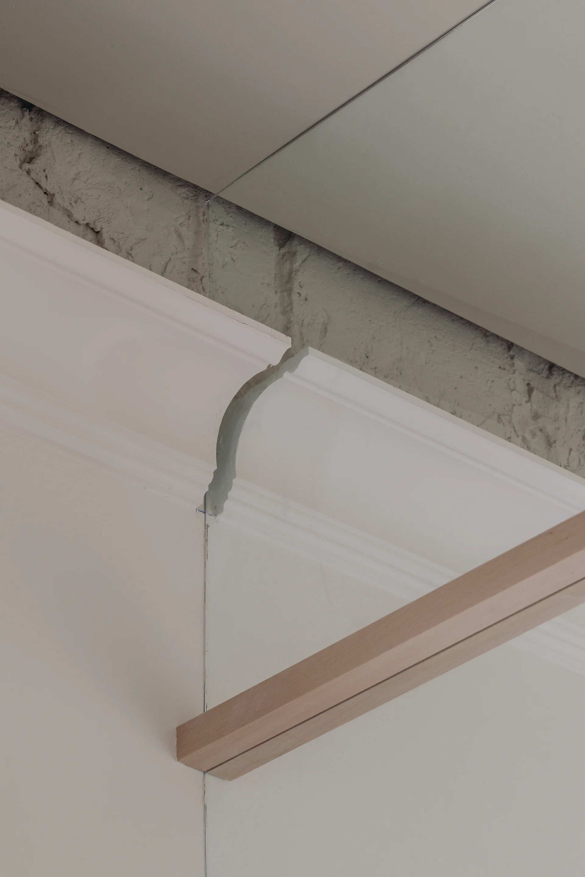 A close-up of off-white crown molding cut to meet a mirrored wall, revealing a textured plaster gap and a light wood rail.