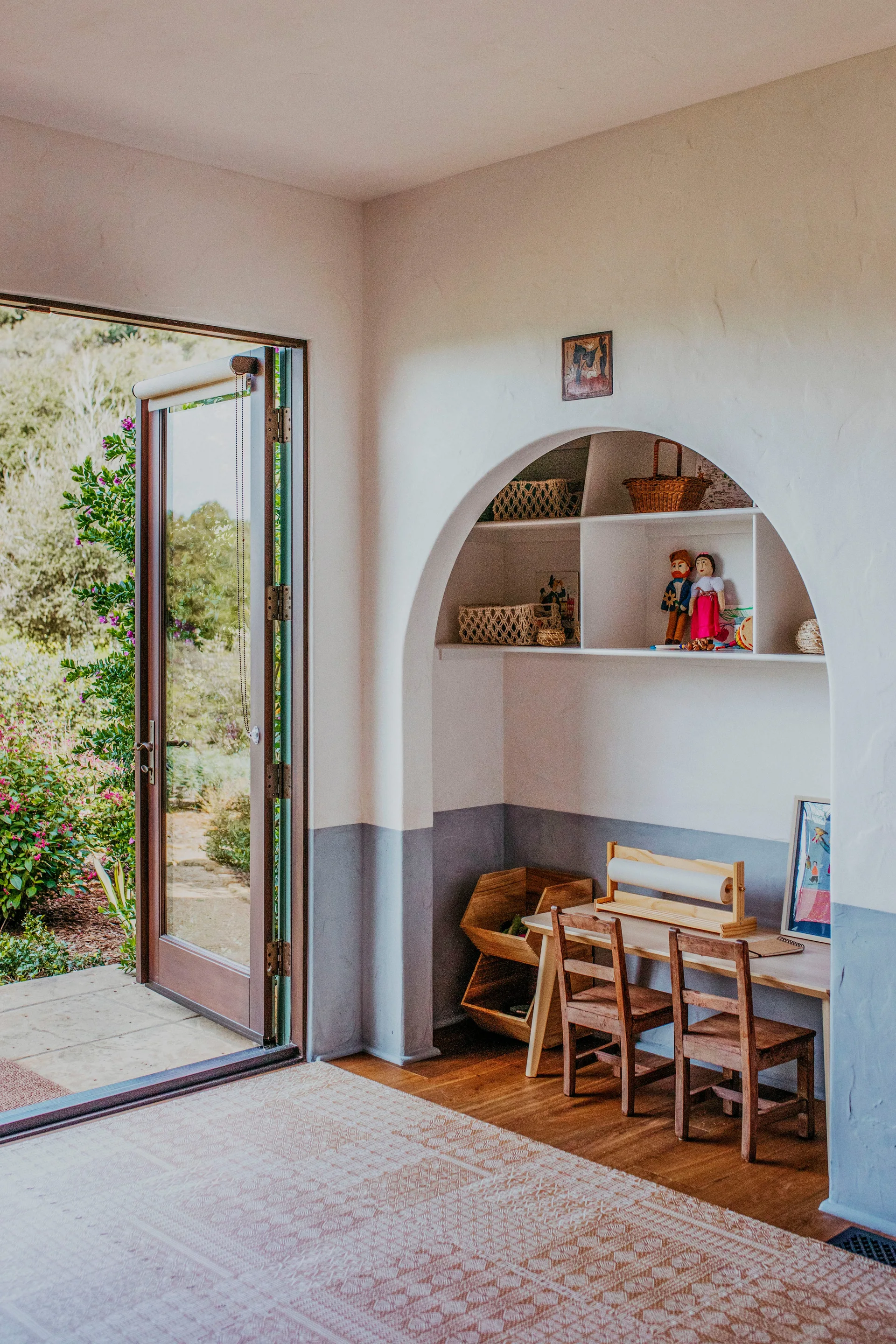 A children's play area features a small wooden table and chairs under a built-in arched alcove next to an open glass door leading to a garden.