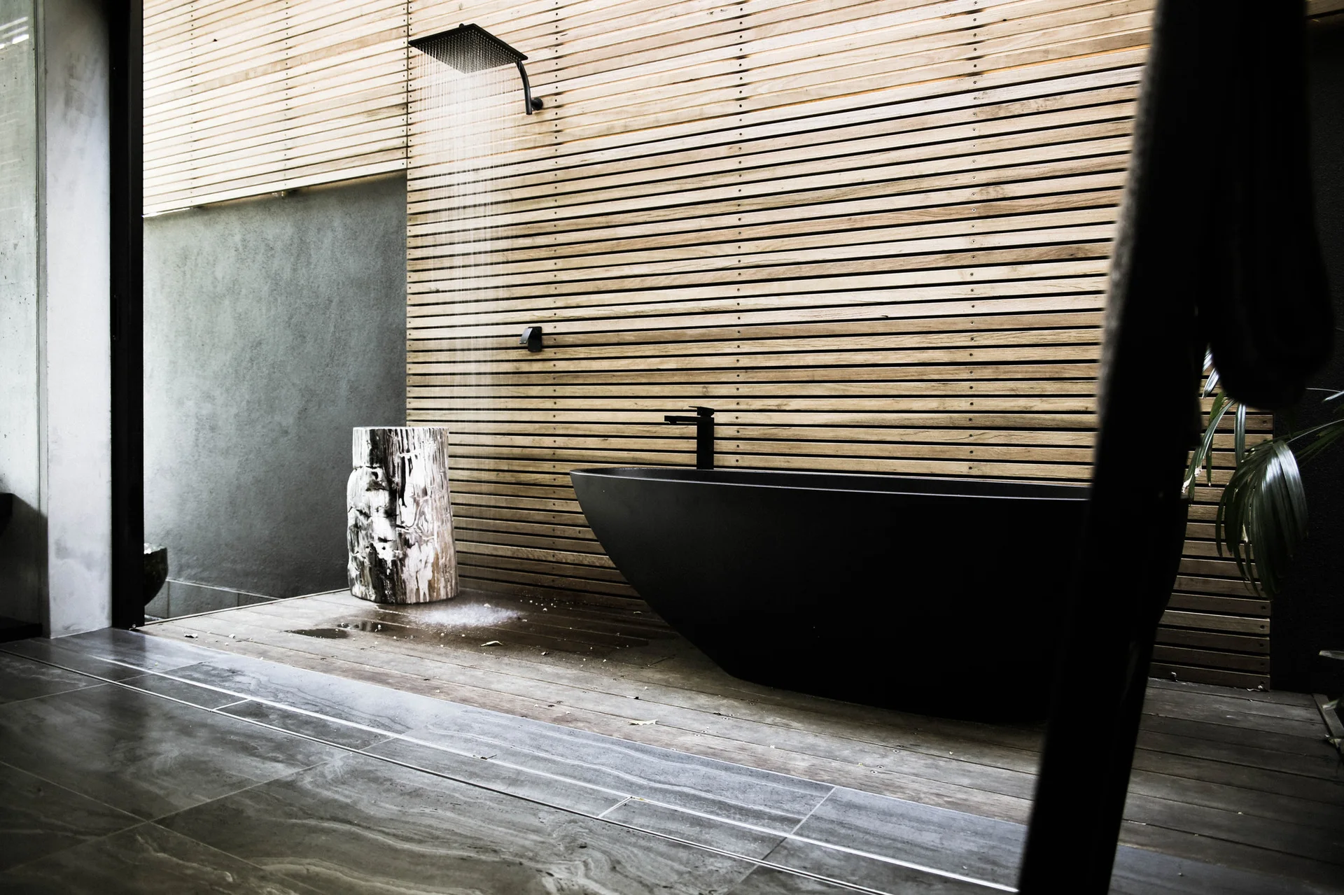 A modern bathroom featuring a matte black freestanding bathtub and wall-mounted shower set against a horizontal slatted wood accent wall.