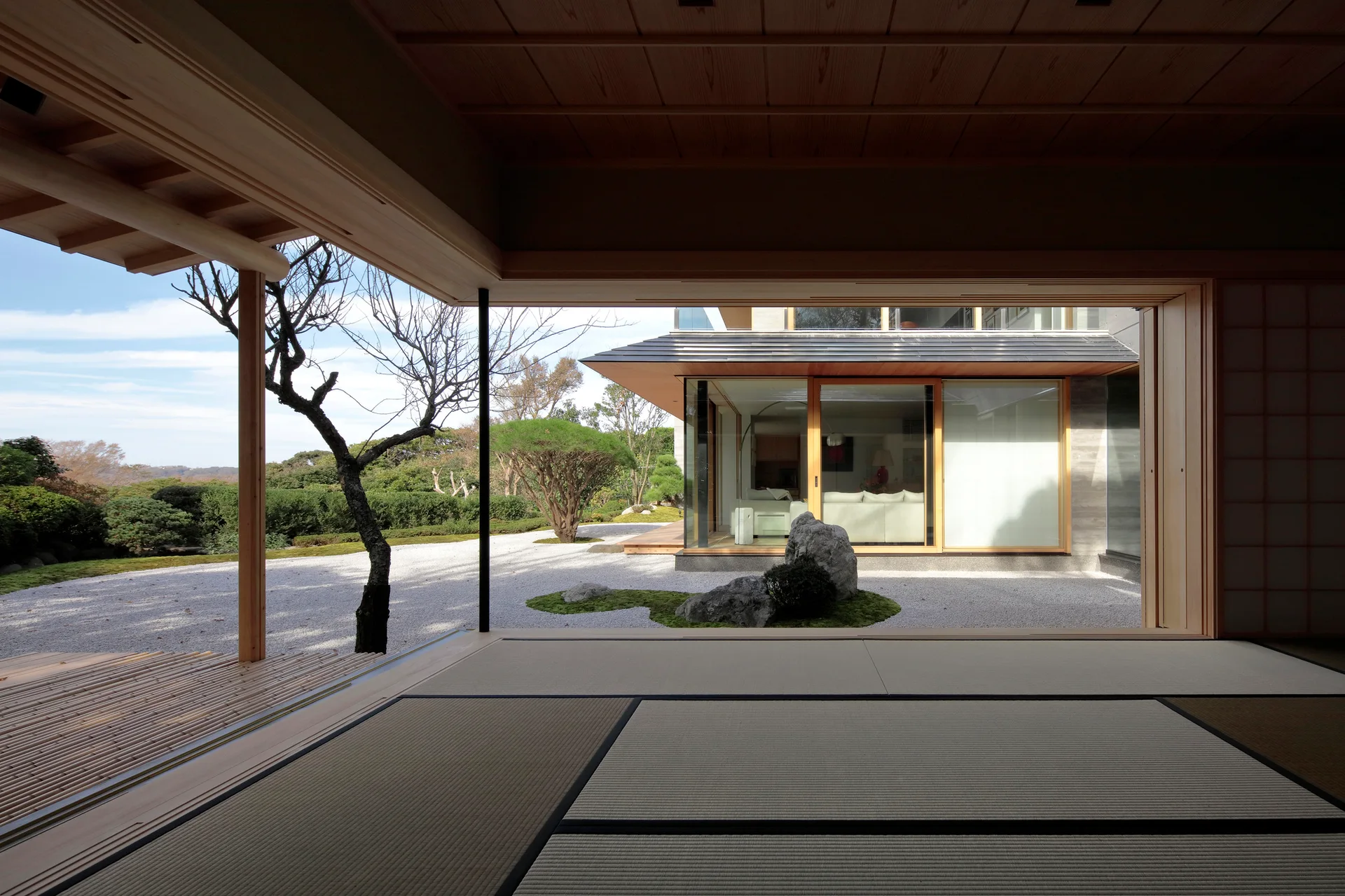 A Japanese washitsu room with tatami mat flooring opens through wide sliding doors onto a gravel zen garden with a central boulder.