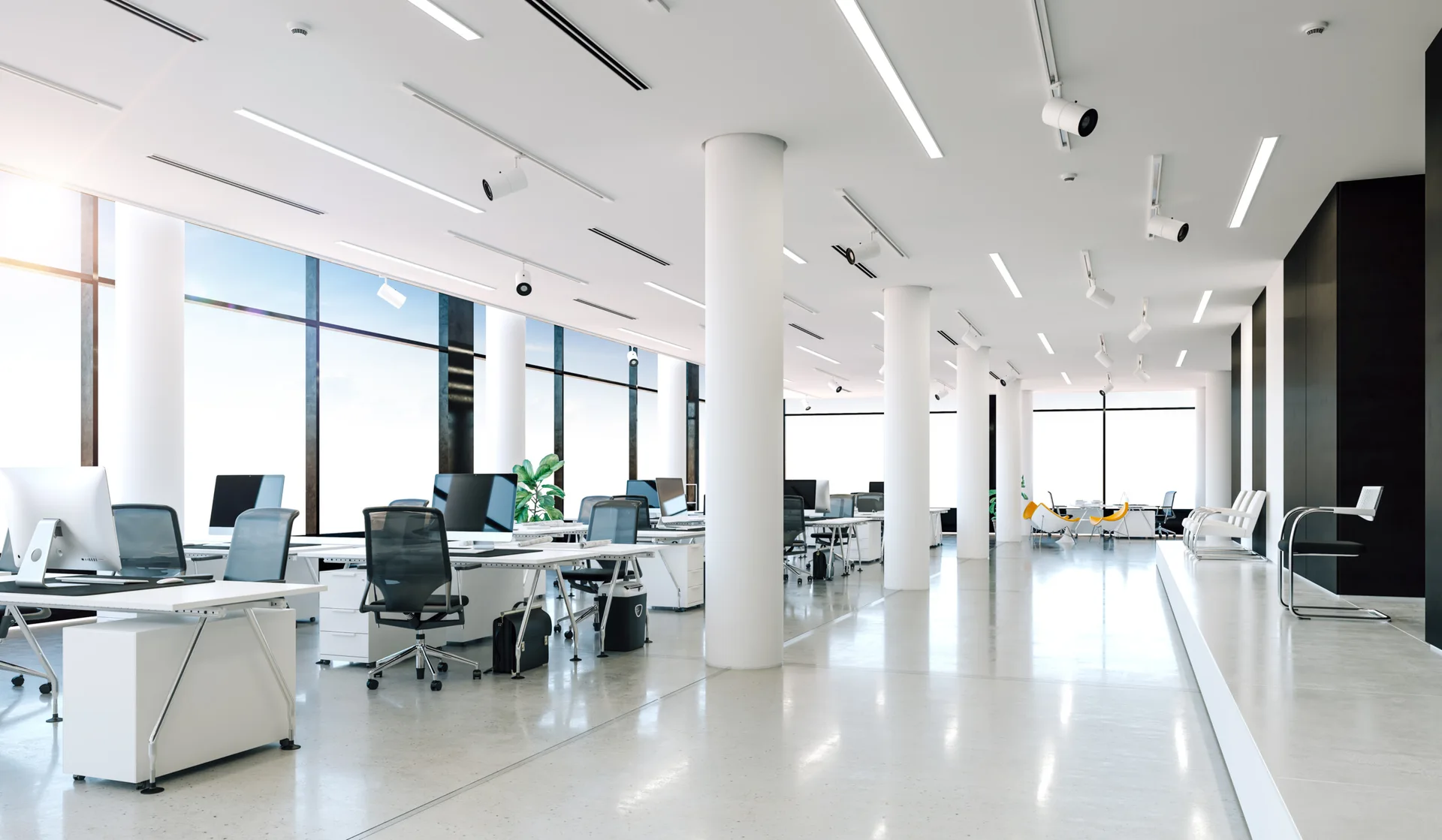 A spacious white open-plan office features rows of white desks, large circular support columns, and polished grey concrete flooring.