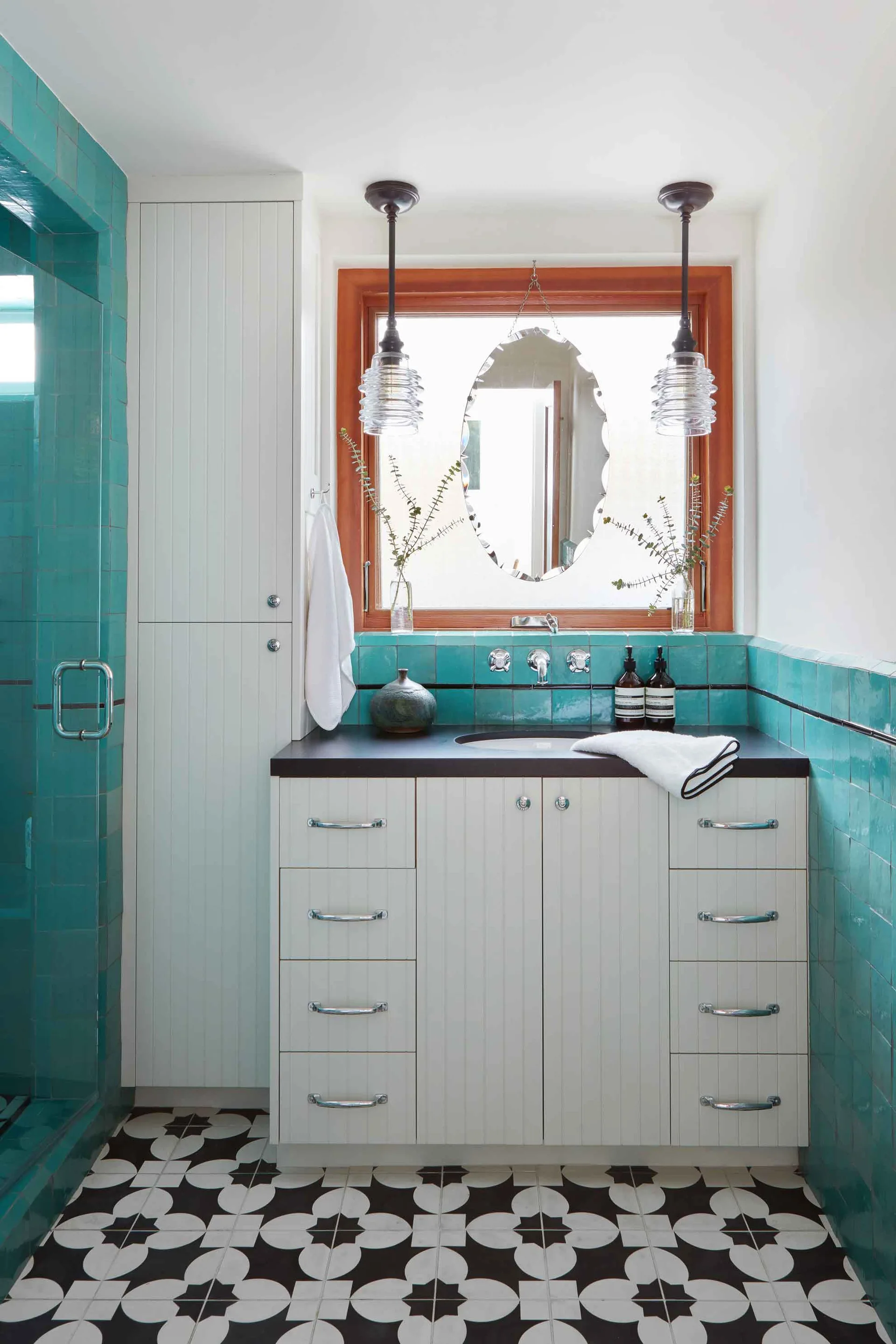 A bathroom features a white beaded-panel vanity with black countertops, vibrant teal wall tiles, and black and white patterned floor tiles.