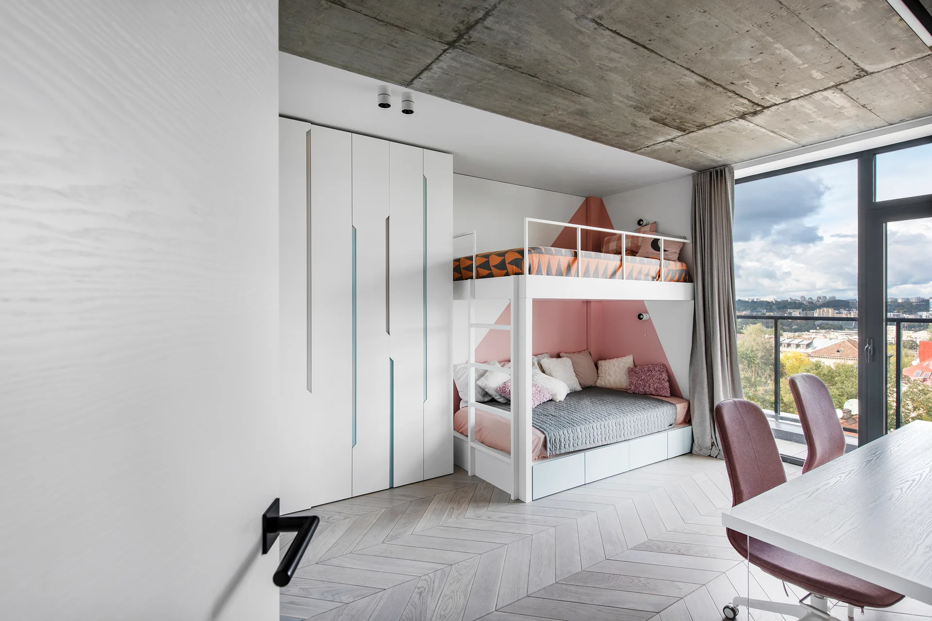 A modern children's bedroom features a white bunk bed, a built-in wardrobe, herringbone flooring, and an exposed concrete ceiling next to a large window.