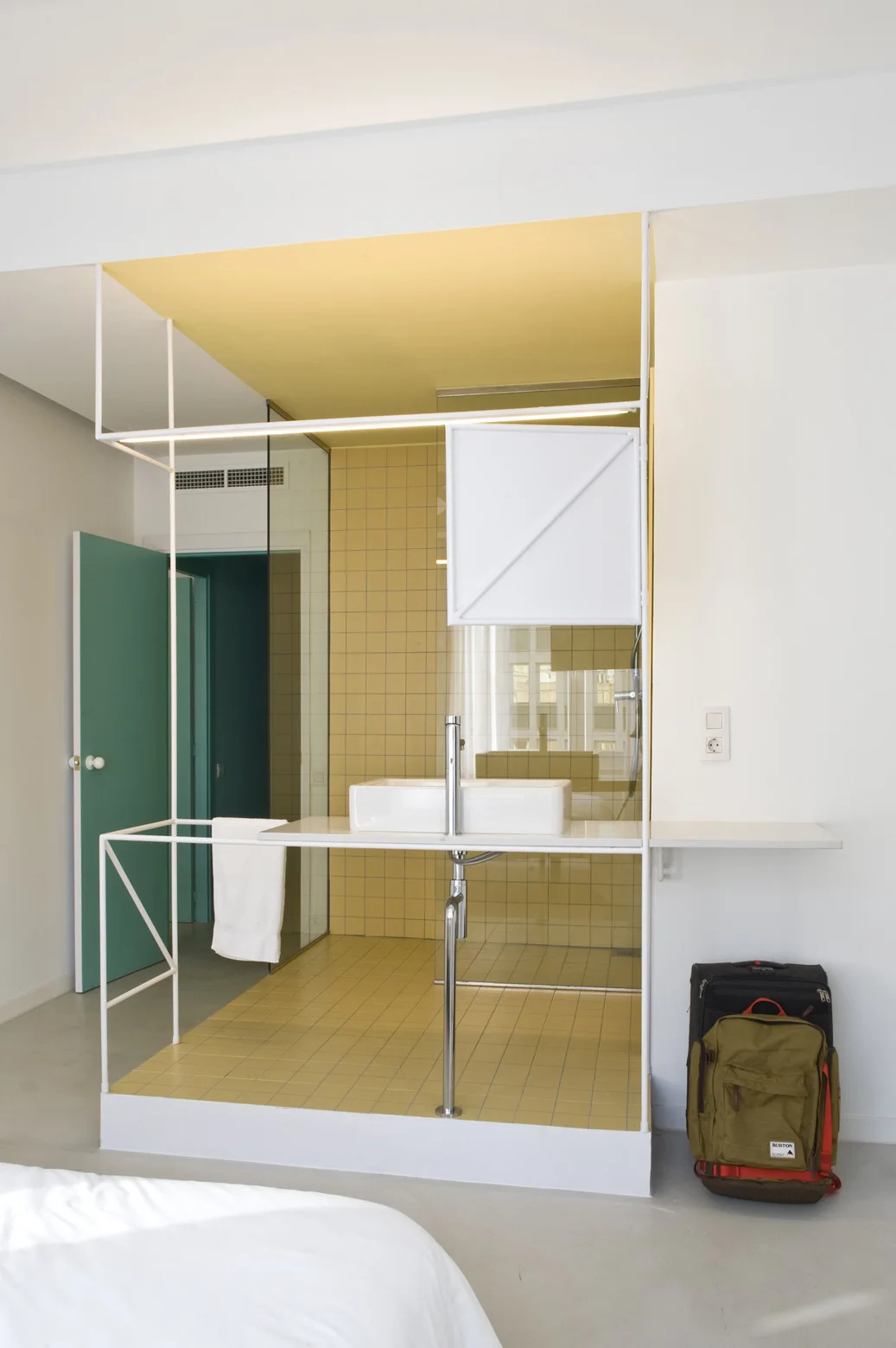 A modern open bathroom features a white vessel sink on a minimalist white metal frame next to a yellow-tiled shower.