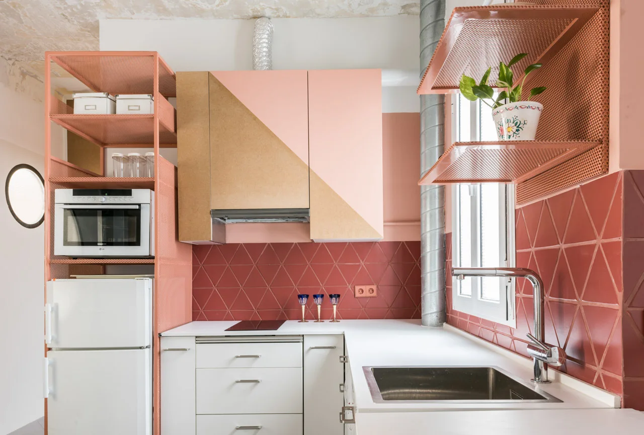 A modern kitchen features a terracotta triangular tile backsplash, pink perforated metal shelving, and a two-toned wood and pink upper cabinet.