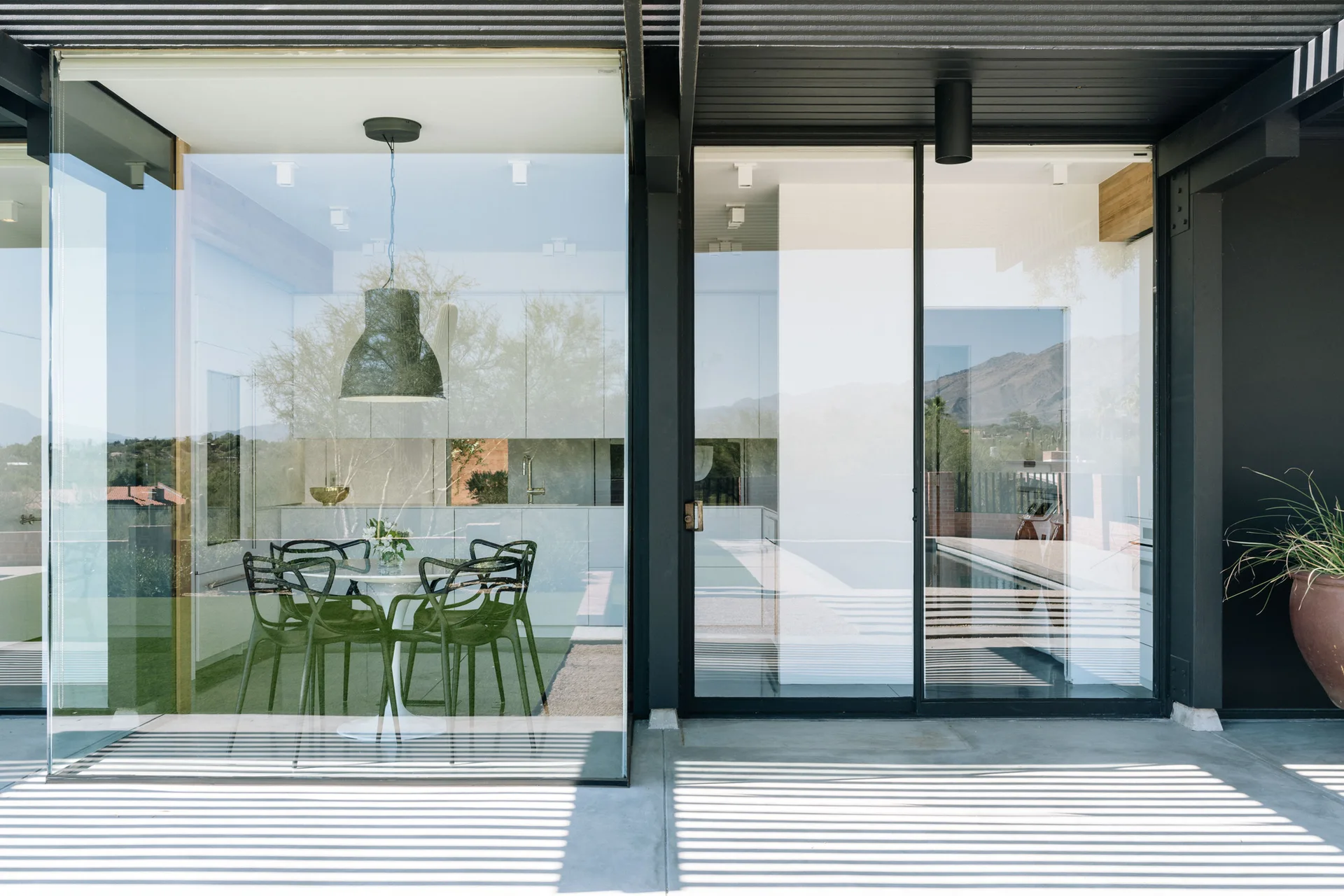 A modern dining room with a white tulip table and black chairs is visible through a large glass wall next to a concrete patio.