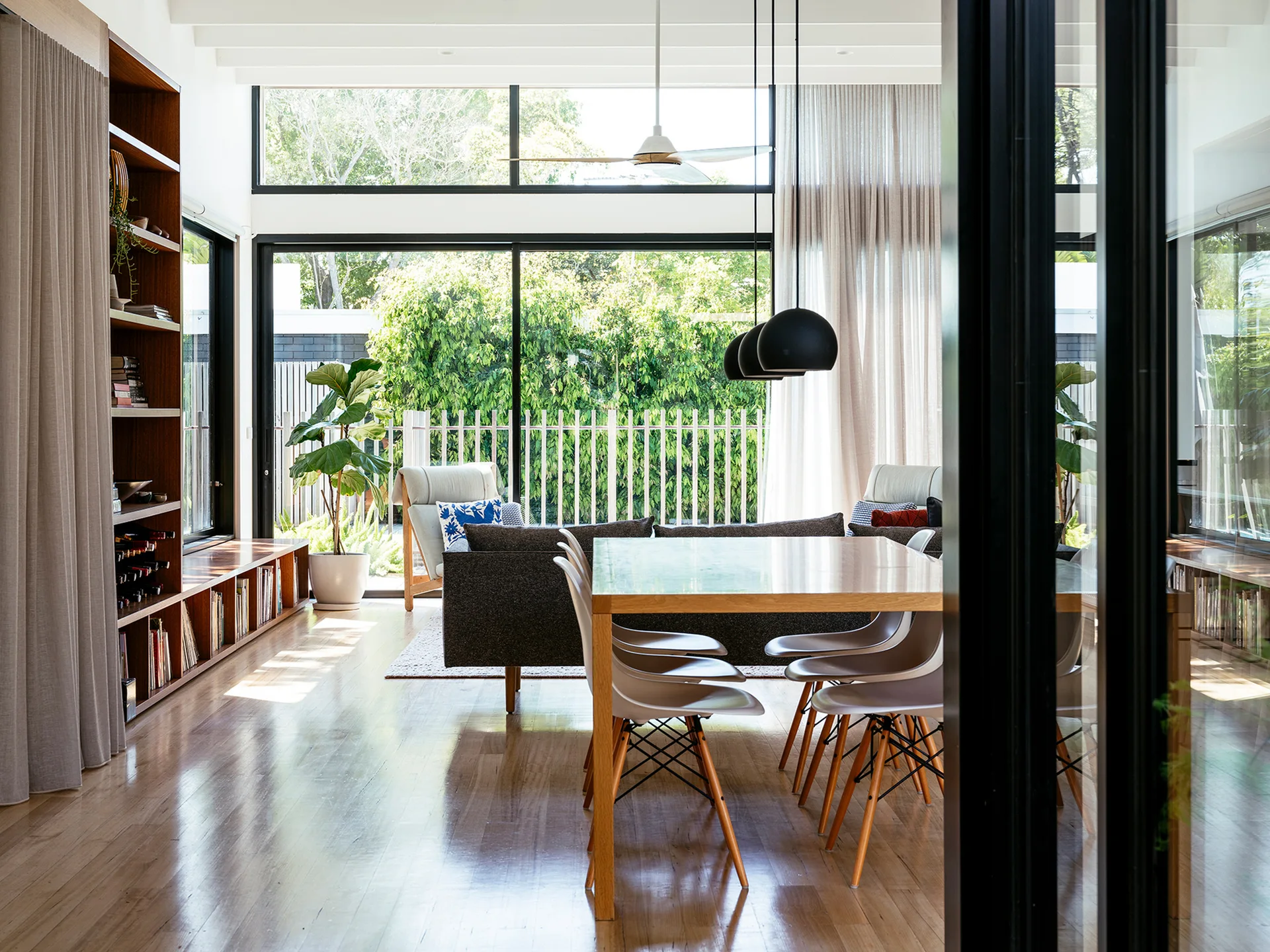 An open dining area features a wooden table with chairs, a dark grey sofa, and a large custom wooden bookshelf unit along the wall.