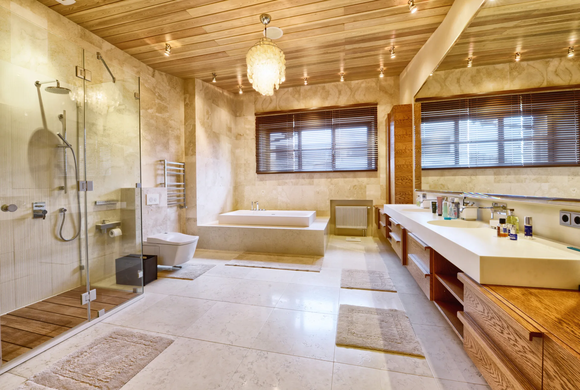 A spacious bathroom with stone-tile walls, a warm wood plank ceiling, a long double vanity, a glass walk-in shower, and a built-in tub.