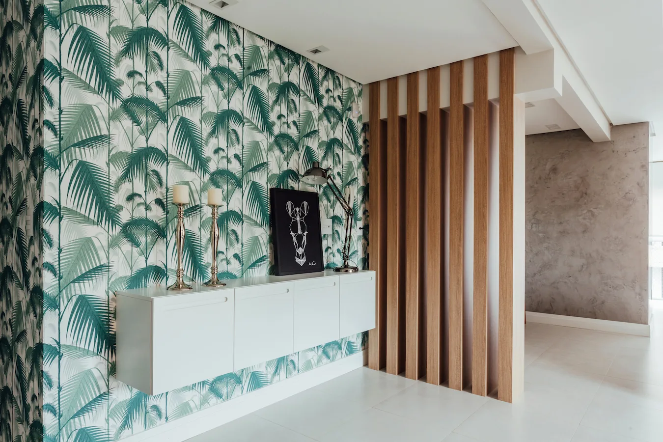 An entryway features green palm-leaf wallpaper, a floating white cabinet with decor, and a vertical wood slat partition wall.