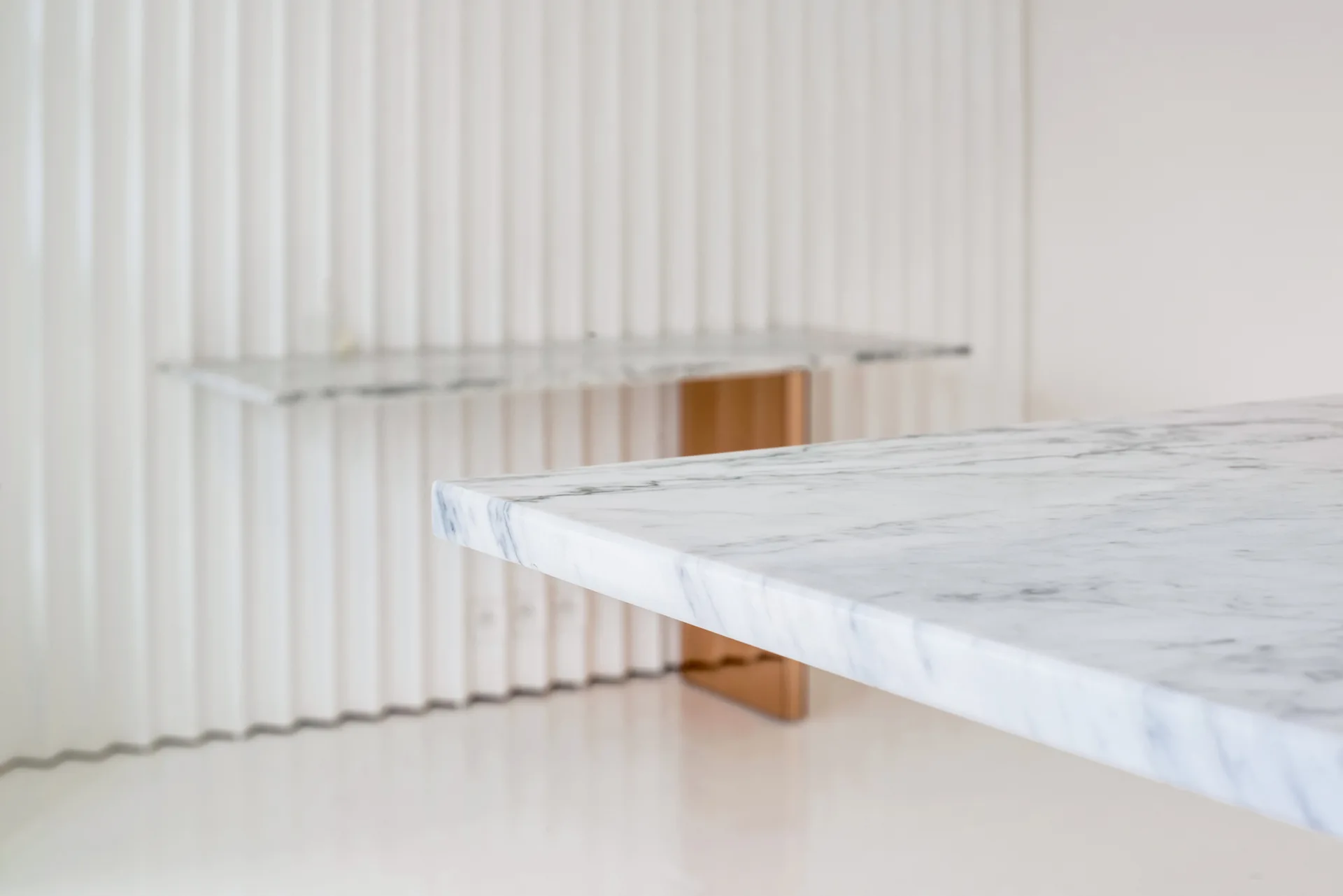 A close-up of a veined white marble table surface with a fluted white wall panel and a wall-mounted console in the background.
