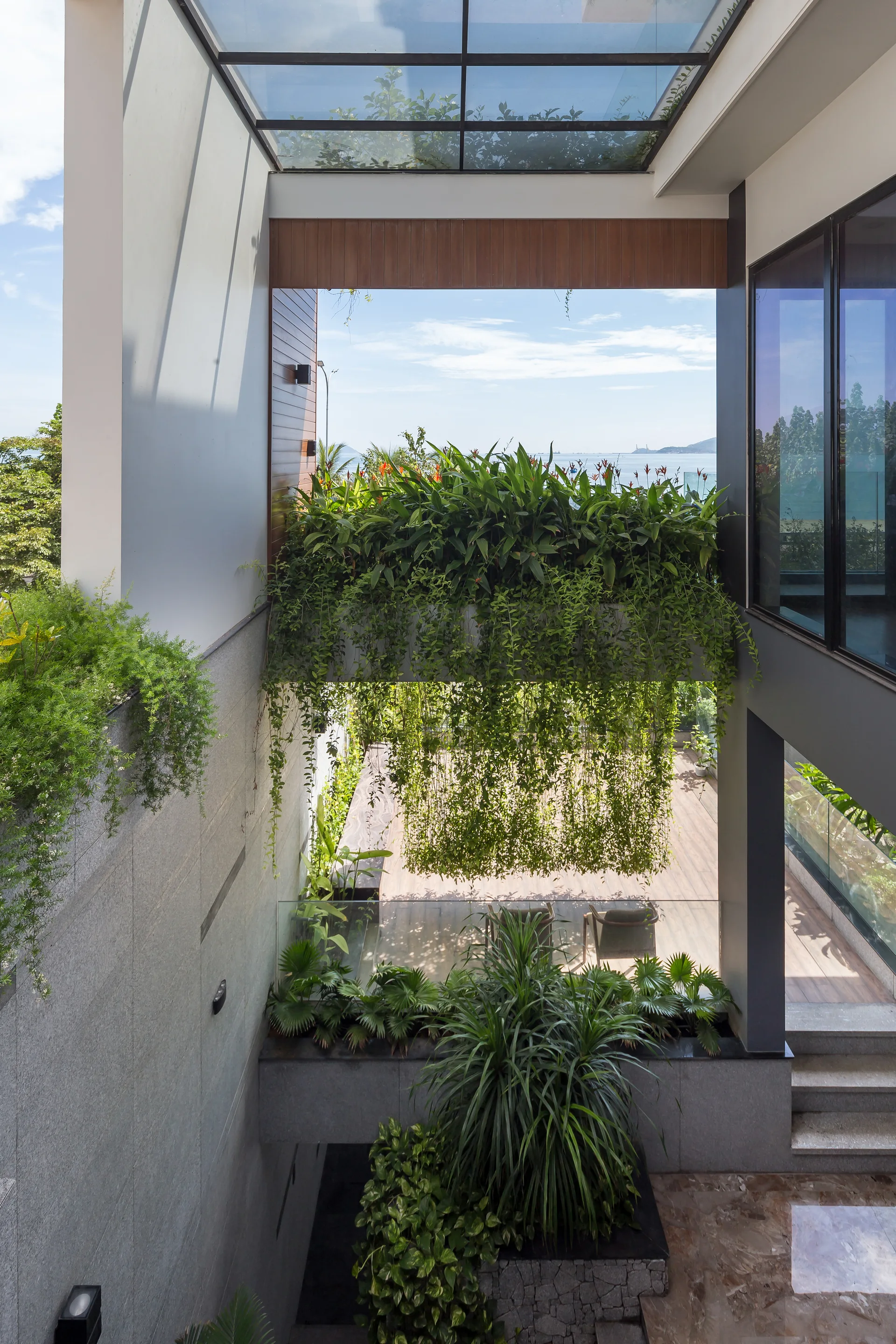 A multi-level outdoor terrace features textured stone walls, wood decking, and lush hanging plants beneath a glass roof.