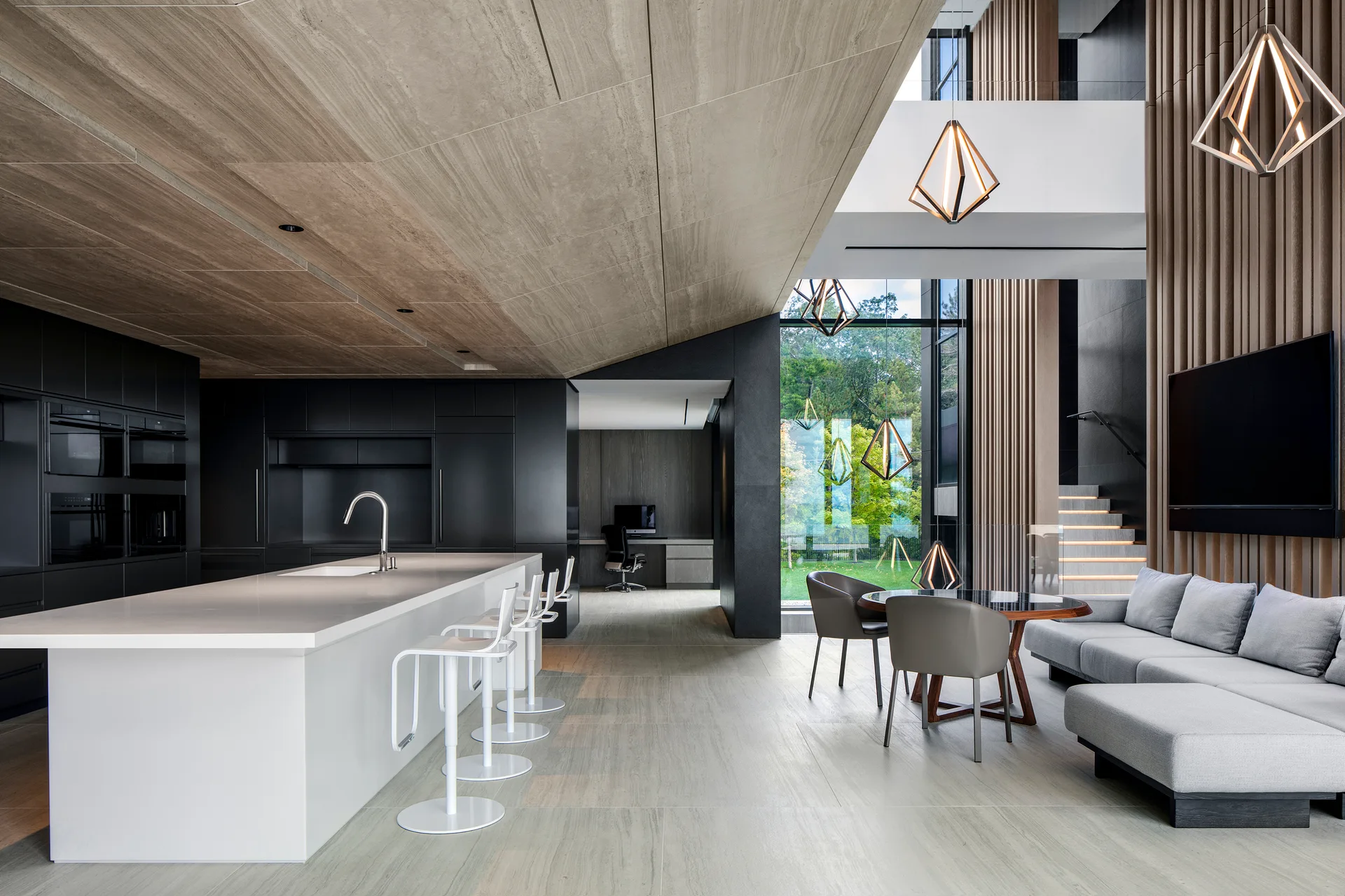A modern open-concept kitchen features a large white island, matte black cabinets, geometric pendant lights, and vertical wood slat wall paneling.