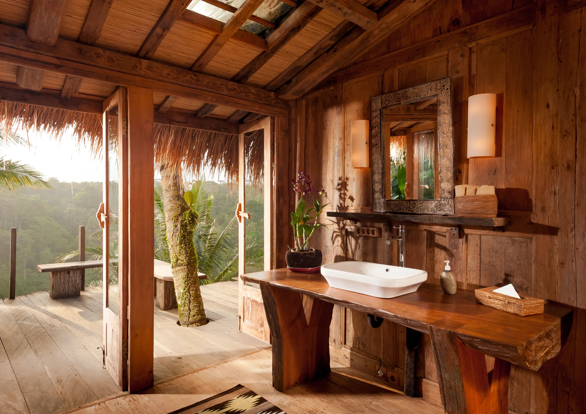 A rustic wooden bathroom features a live-edge wood vanity with a white vessel sink, a carved mirror, and open doors leading to an outdoor deck.