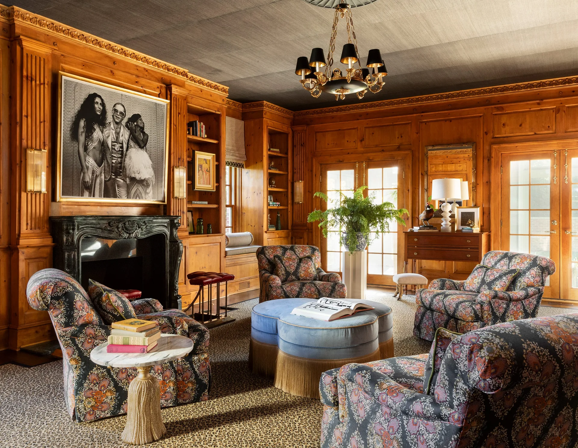 A traditional wood-paneled library with patterned armchairs surrounding a blue clover-shaped ottoman on a leopard-print carpet.