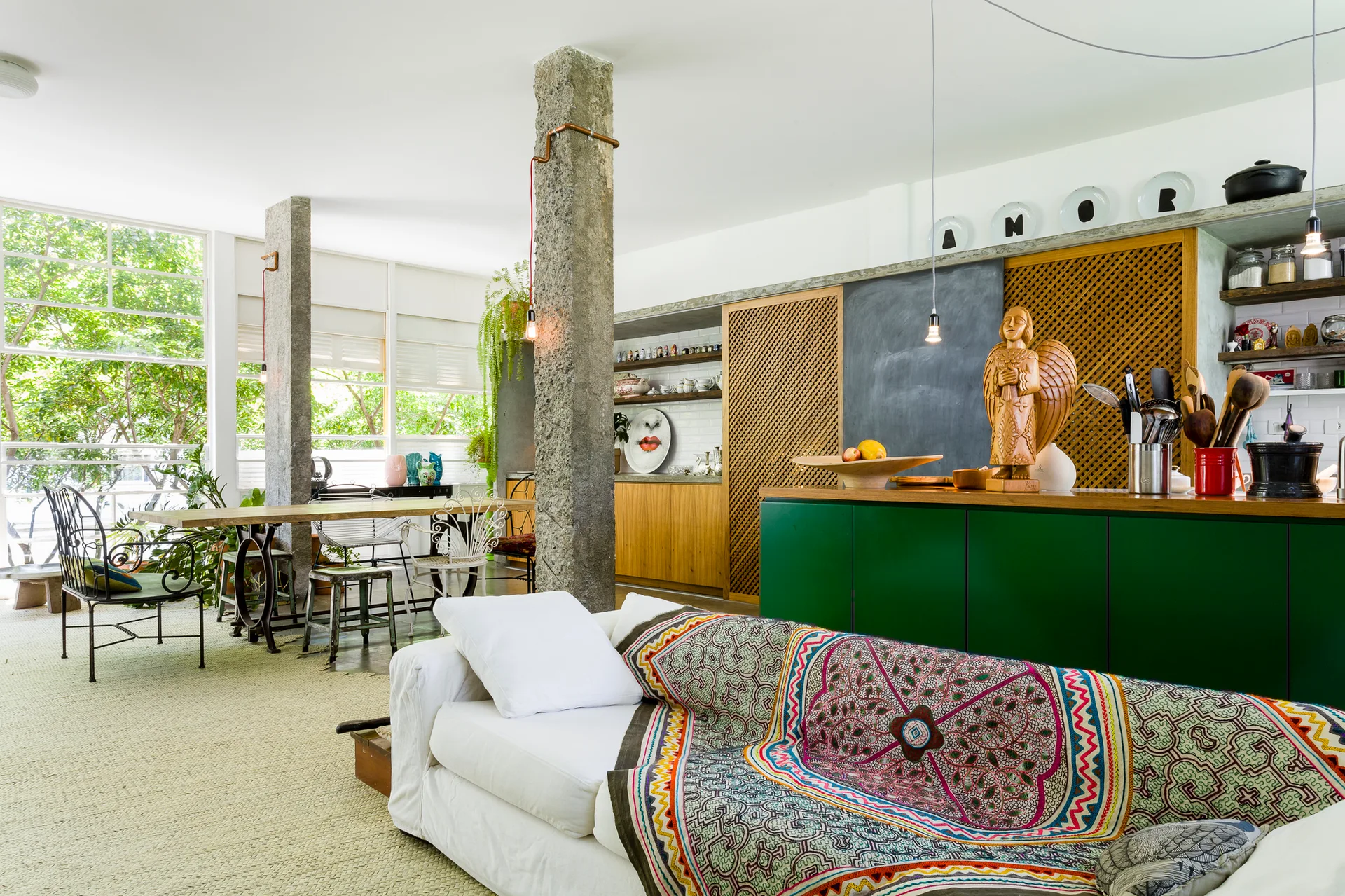 An open-concept living area features rough stone columns, a white sofa draped in a patterned throw, and a green kitchen island.