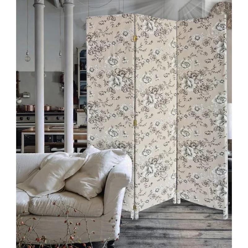A three-panel beige fabric folding screen with a black floral pattern stands next to a white linen sofa on a wood floor.
