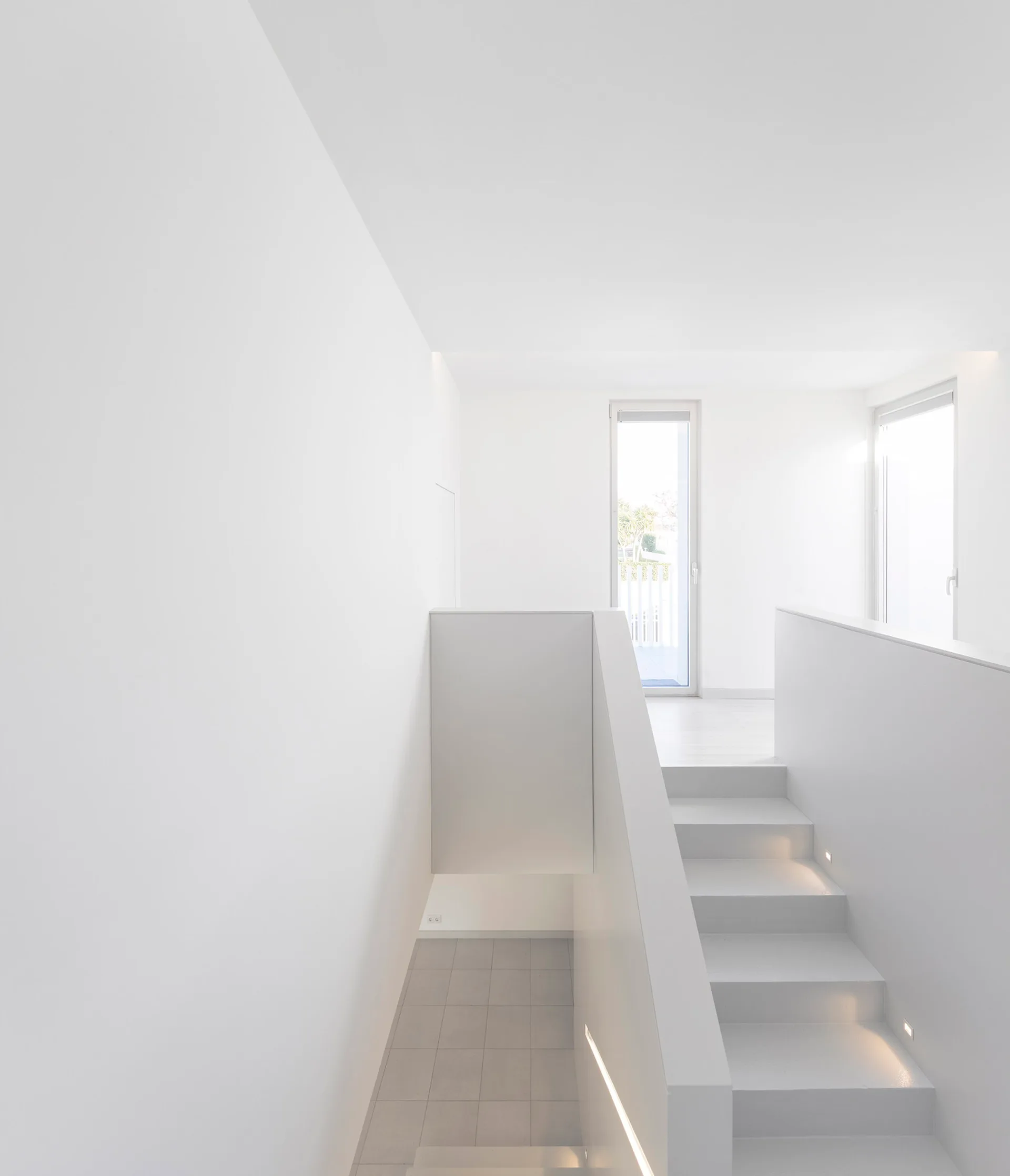 A bright white minimalist staircase features a solid white balustrade wall and small integrated step lights along the treads leading to a landing.