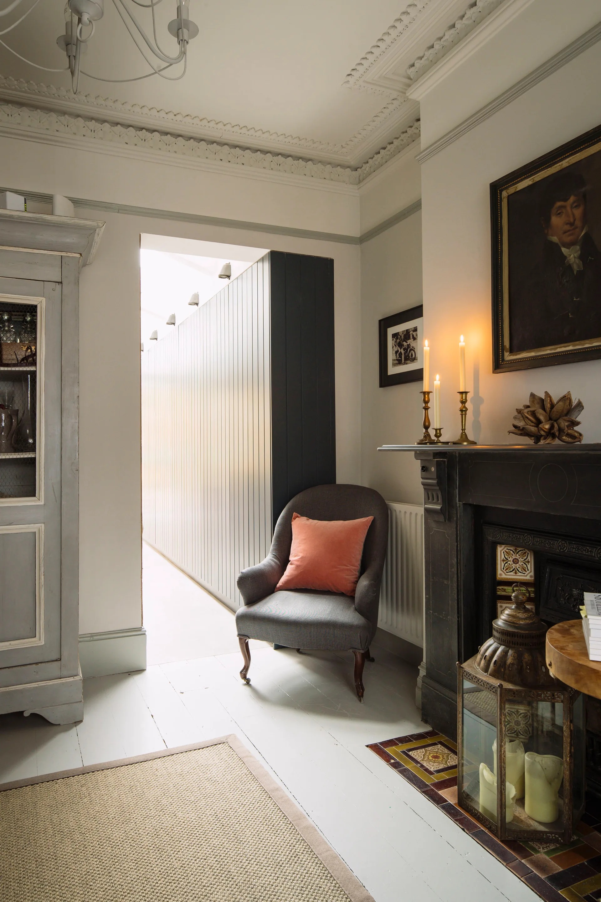 A classic living room corner featuring a dark grey armchair with a peach pillow next to a black fireplace with candles on the mantle.