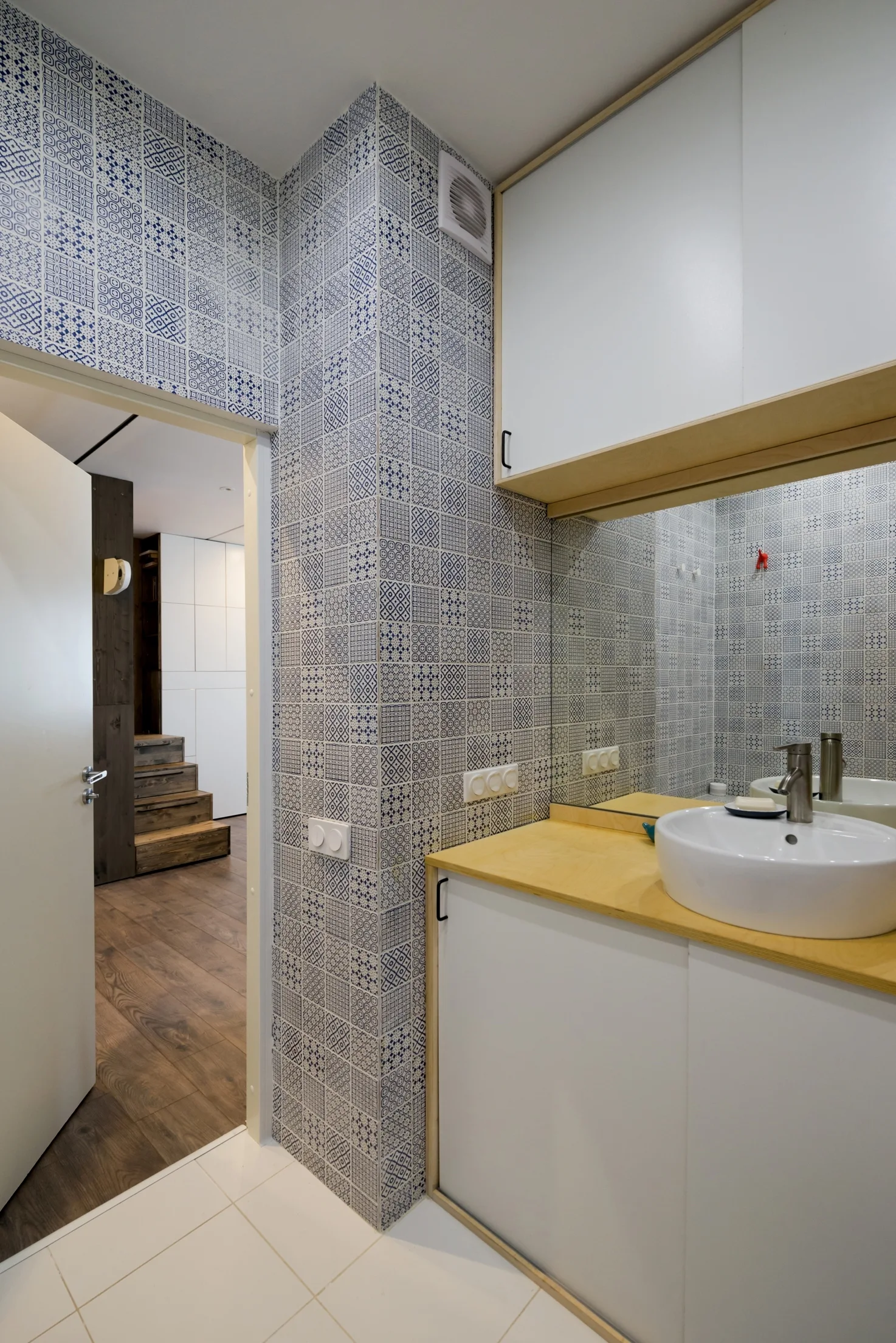 A small bathroom featuring blue and white patterned wall tiles, a white vanity with a light wood countertop, and a white vessel sink.