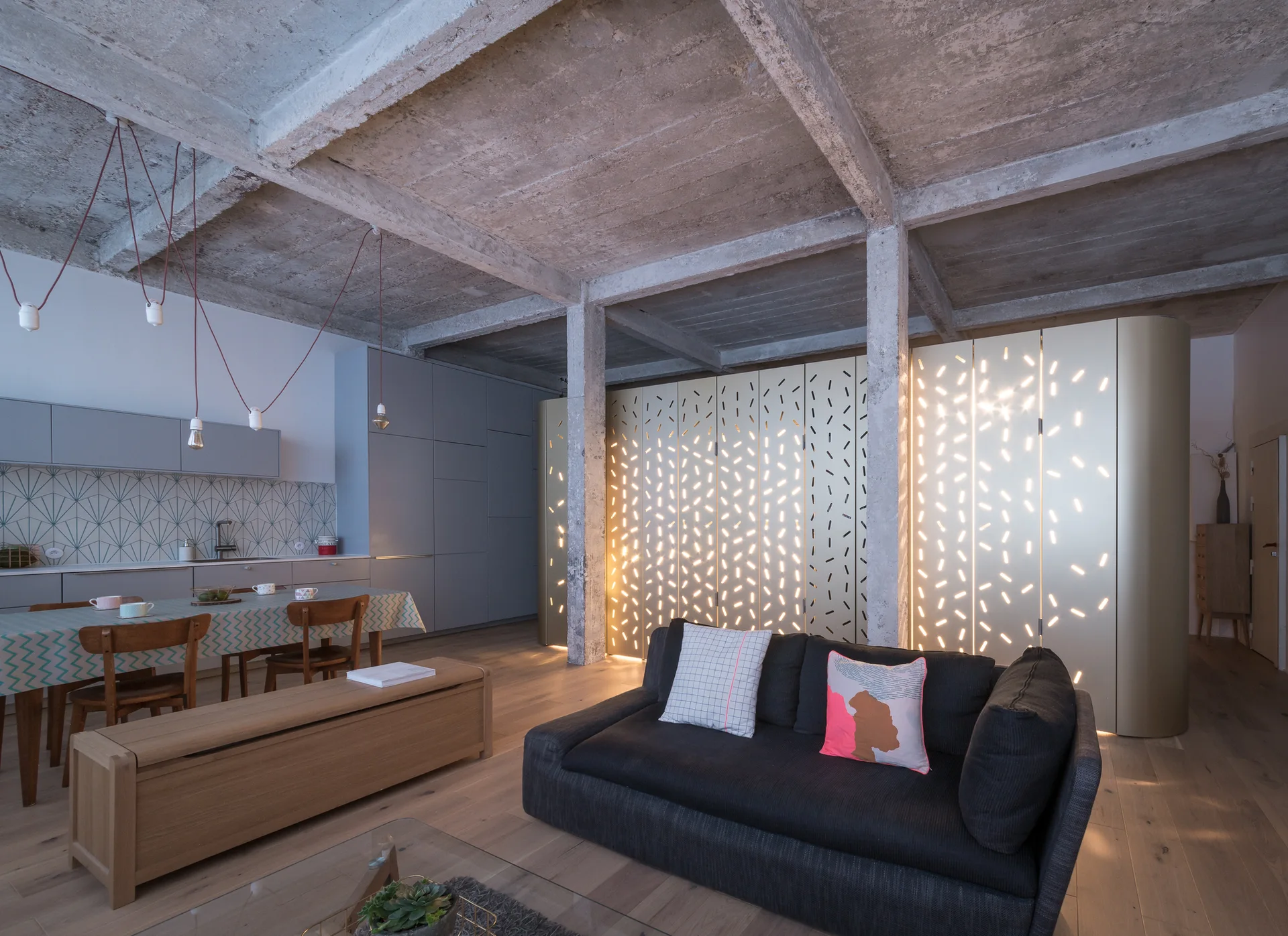 An industrial loft interior with an exposed concrete ceiling, a charcoal sofa, and a large backlit gold perforated screen partition.