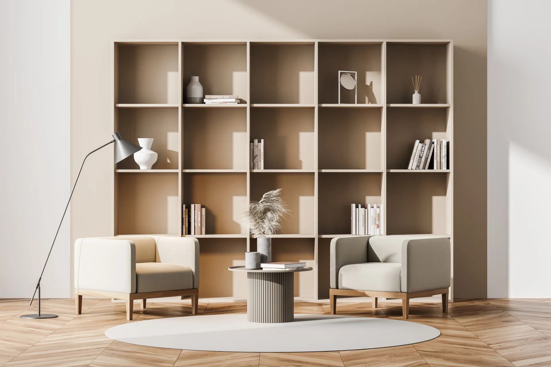 Two beige armchairs flank a fluted coffee table in front of a tall tan bookshelf on herringbone wood floors.