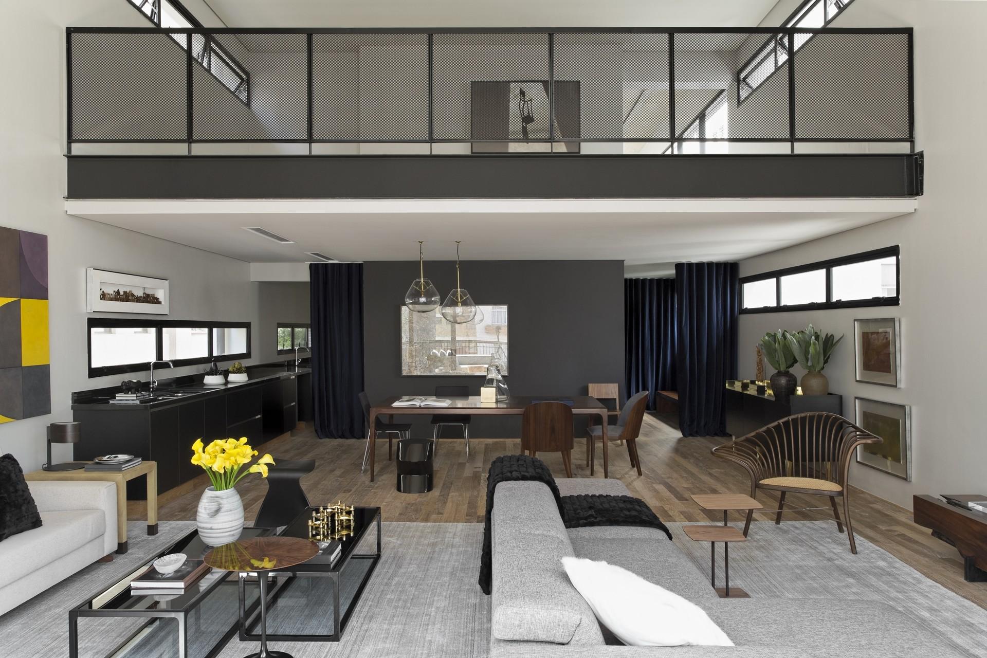 An open concept living room with a grey sofa, a wood dining table, and a mezzanine level featuring a black mesh railing.