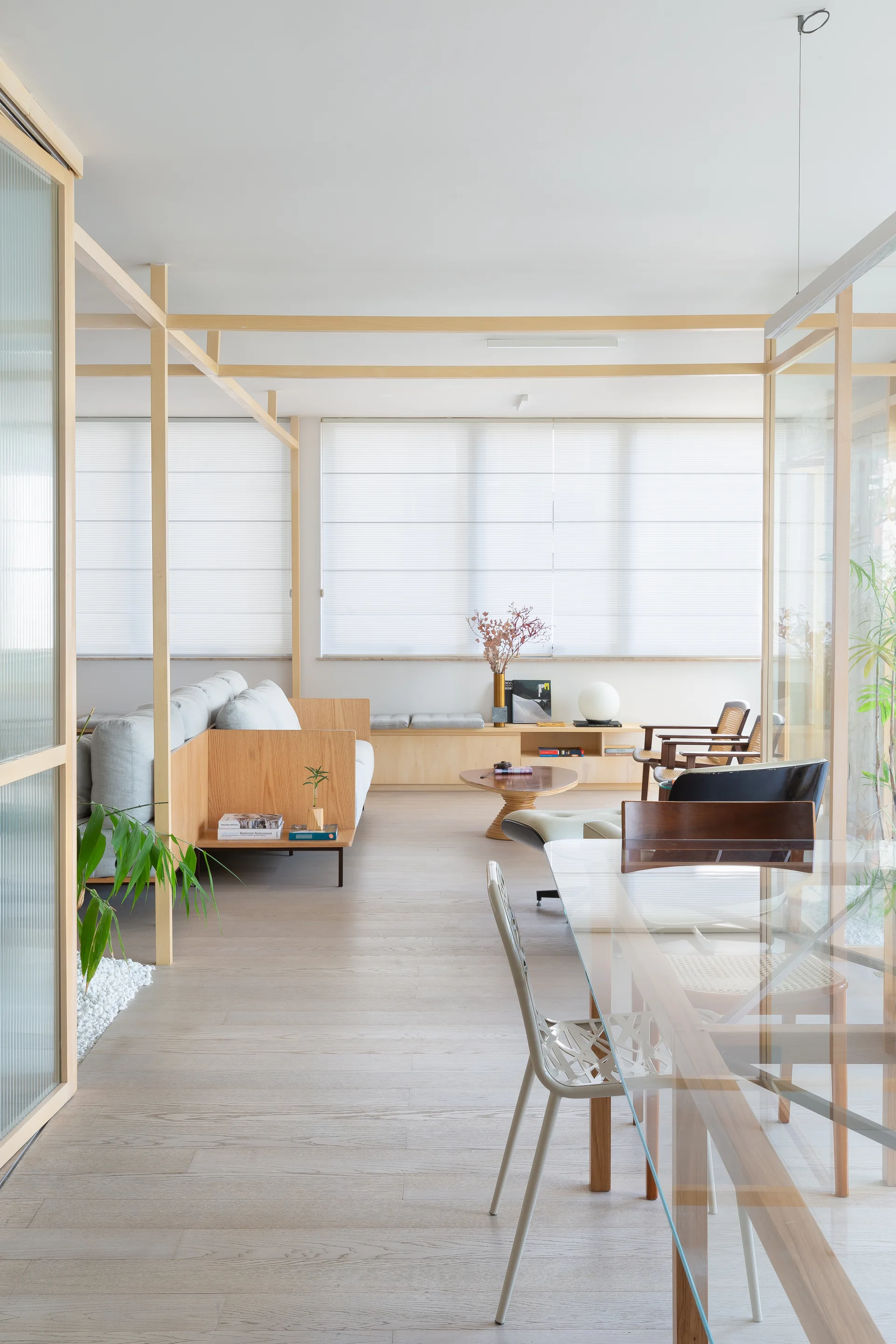 An open living and dining area featuring a light grey sofa, glass table, and pale wood post-and-beam frame structure.