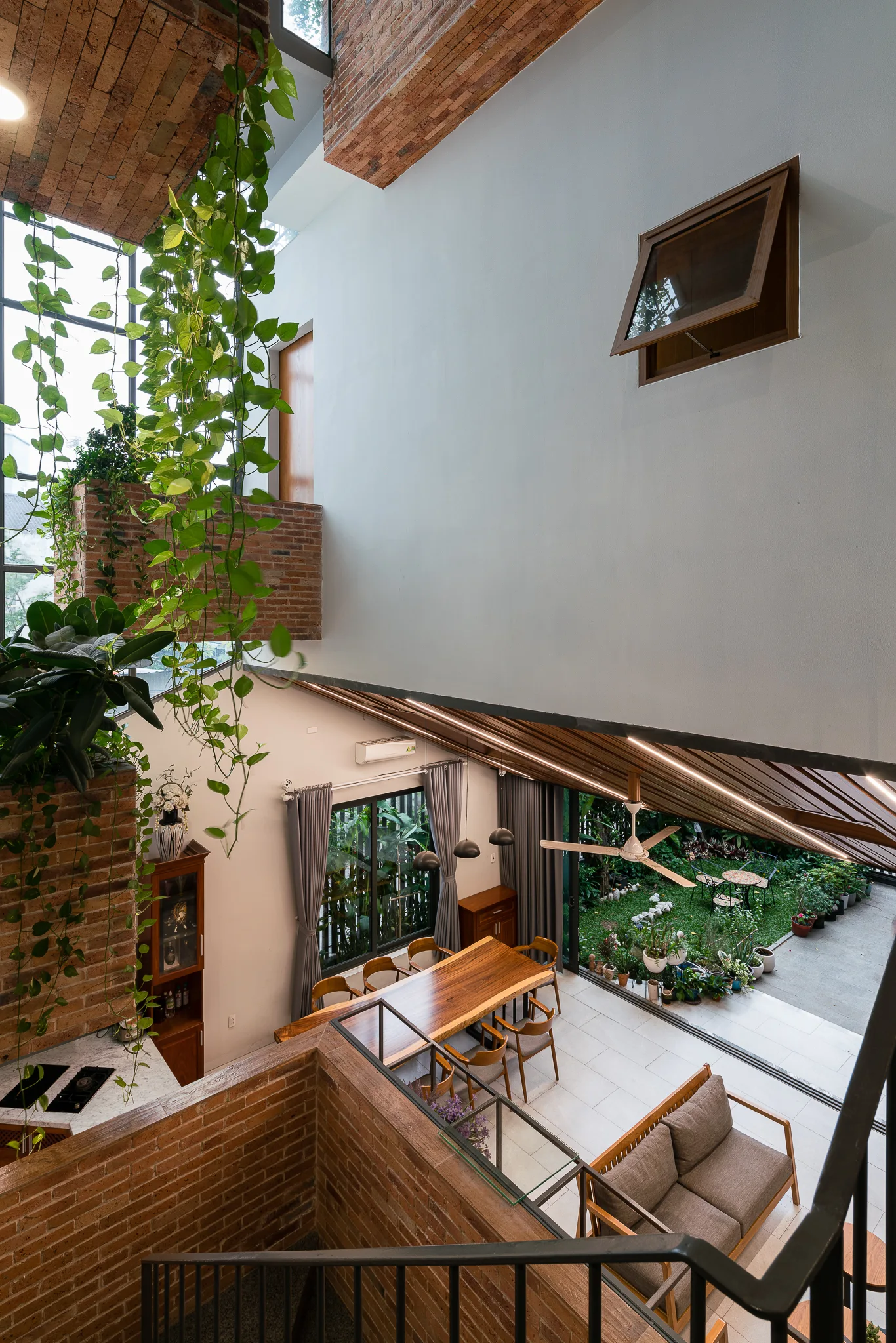 A high-angle view of a dining area with a wood slab table, exposed brick walls, and cascading green vines from a mezzanine.