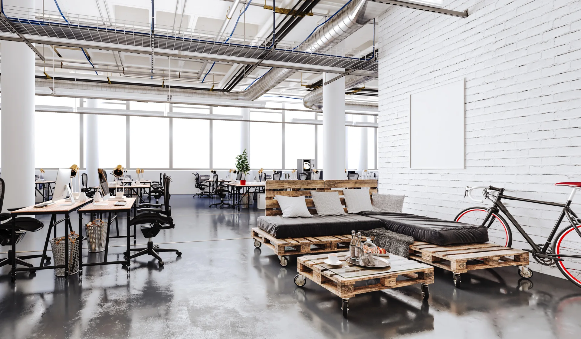 An open office workspace with a custom wood pallet sectional sofa and coffee table sitting beside a white painted brick wall.