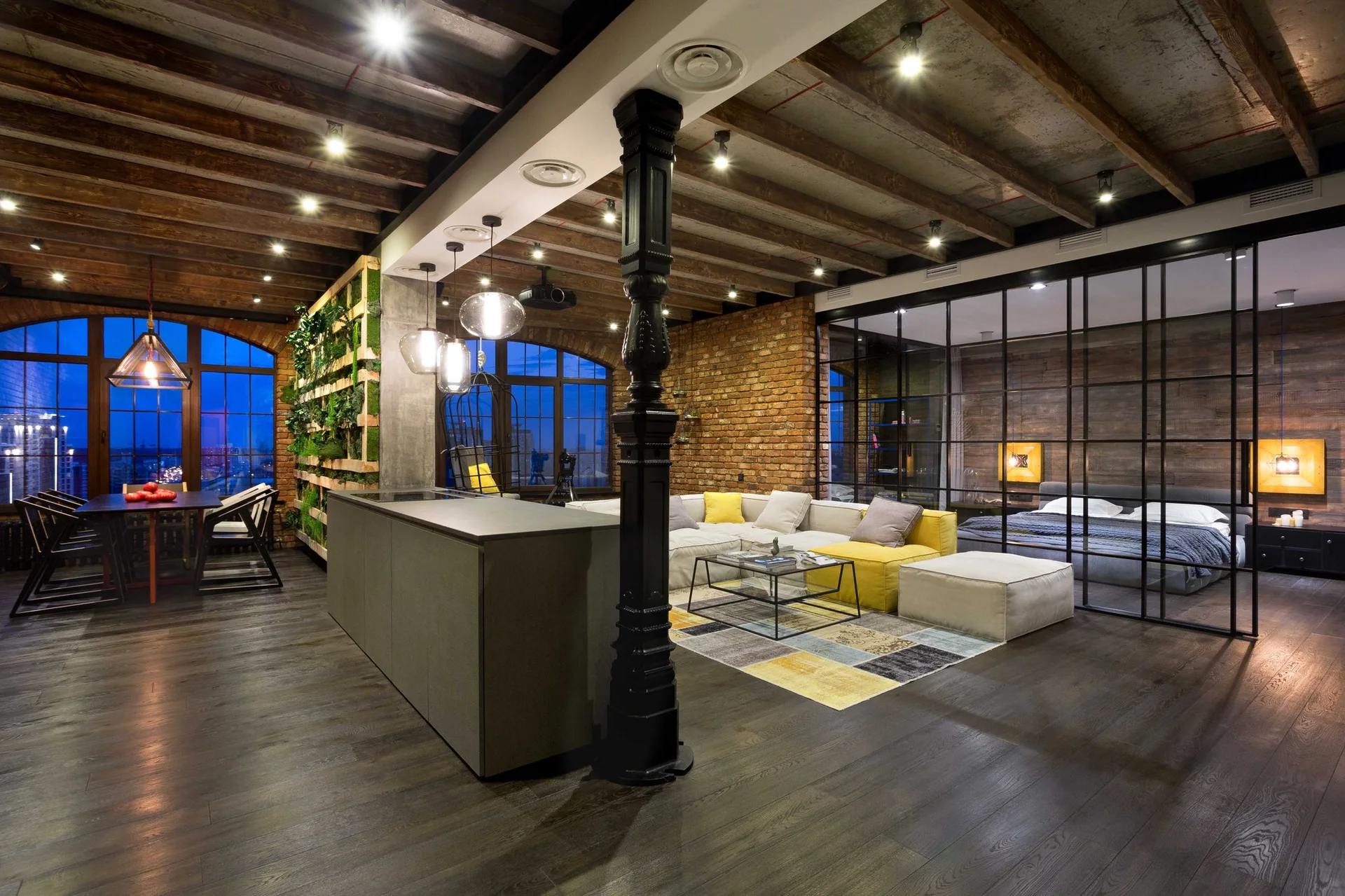 An industrial open-plan loft living room features a black metal glass partition, exposed brick walls, and dark wooden ceiling beams.