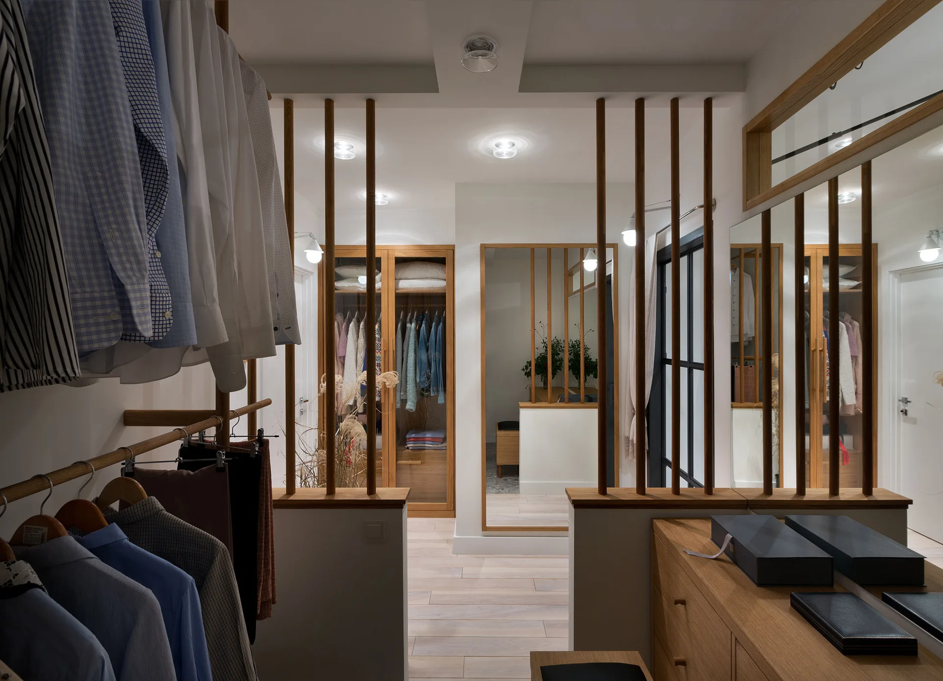 A walk-in closet featuring light wood cabinetry, clothing racks, and vertical wooden slat dividers separating the dressing areas.