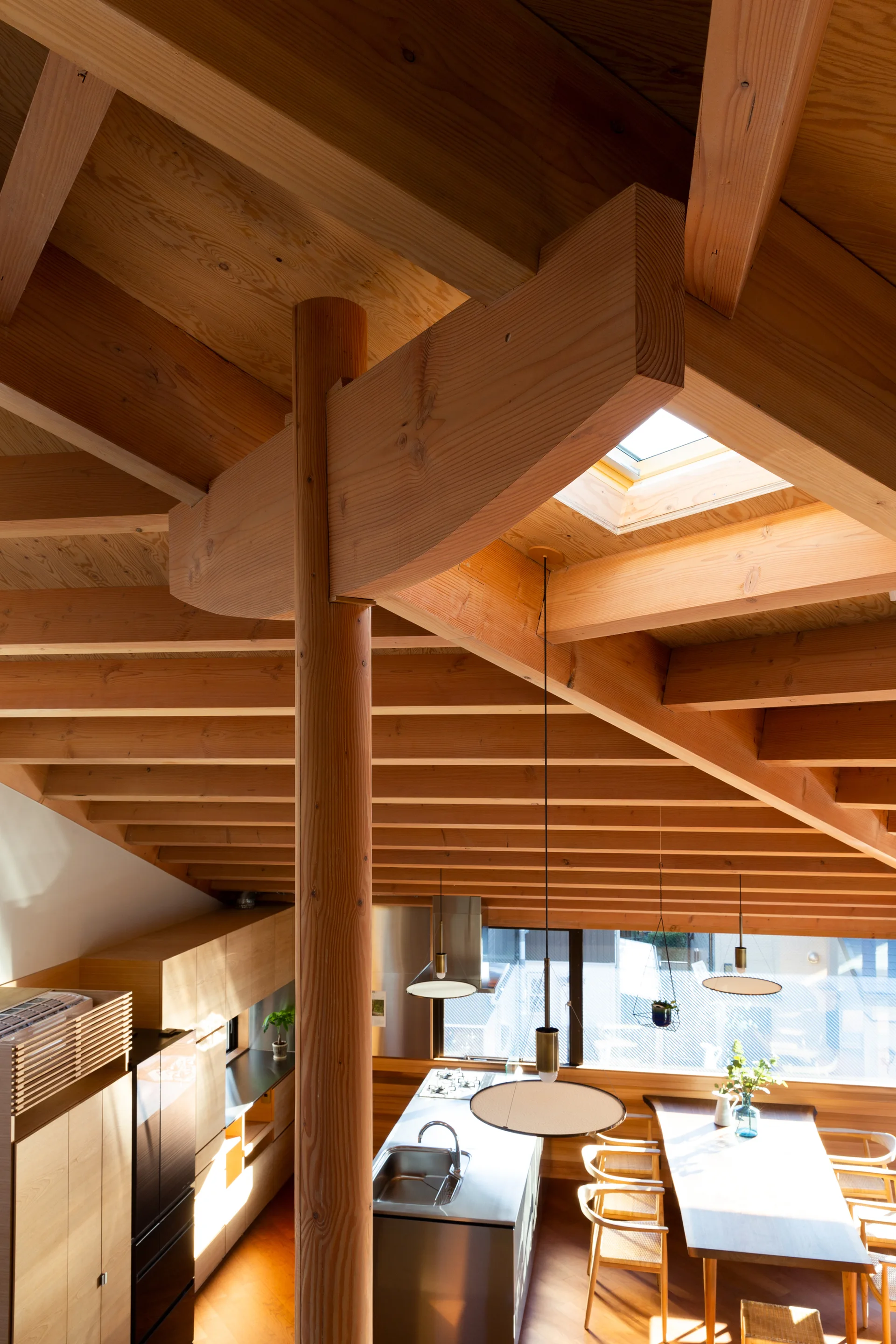 A modern open-plan kitchen and dining area features an exposed timber-beamed ceiling, a skylight, a wooden support post, and a stainless steel island.