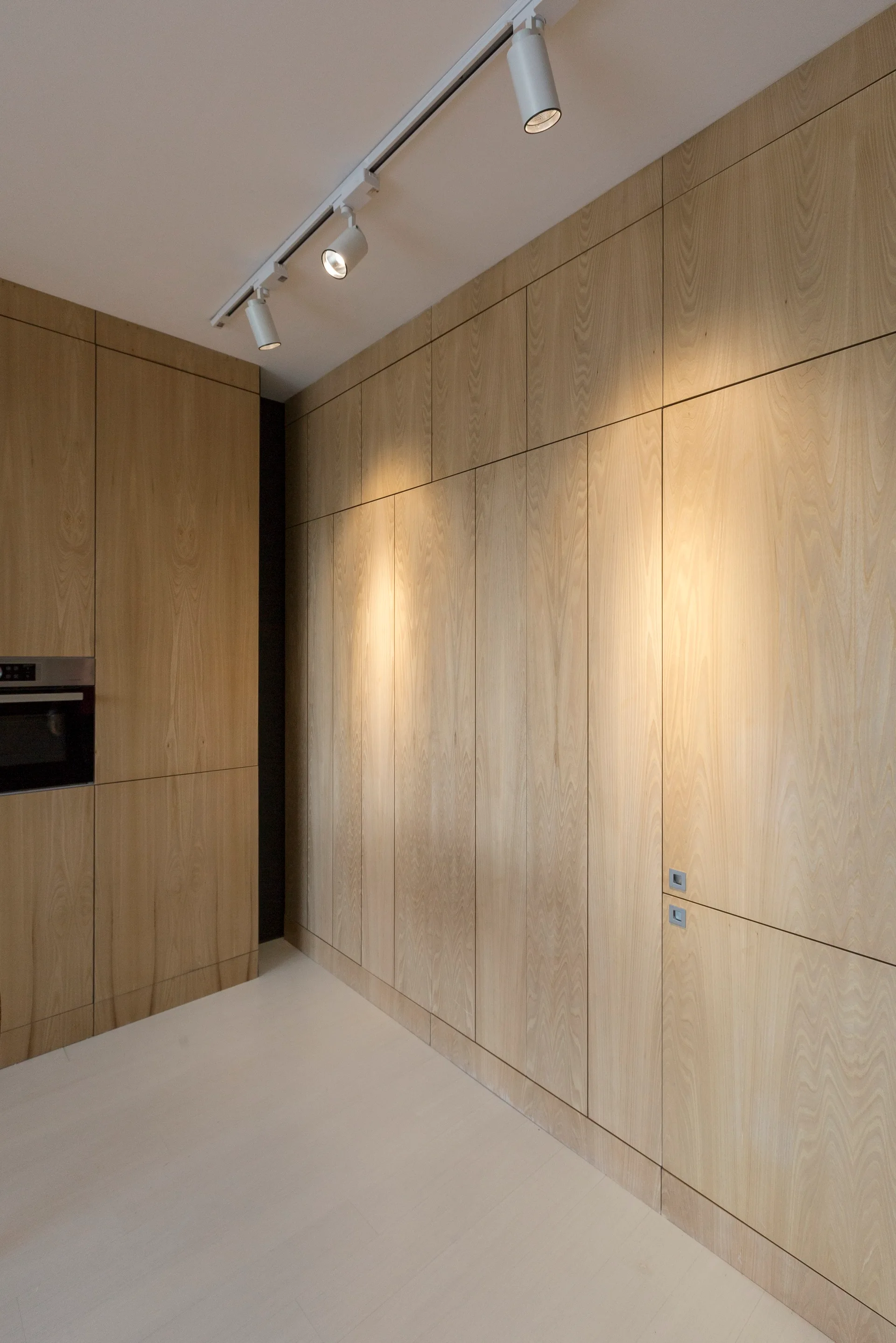Seamless light wood grain floor-to-ceiling kitchen cabinets with a built-in oven and white overhead track lighting.