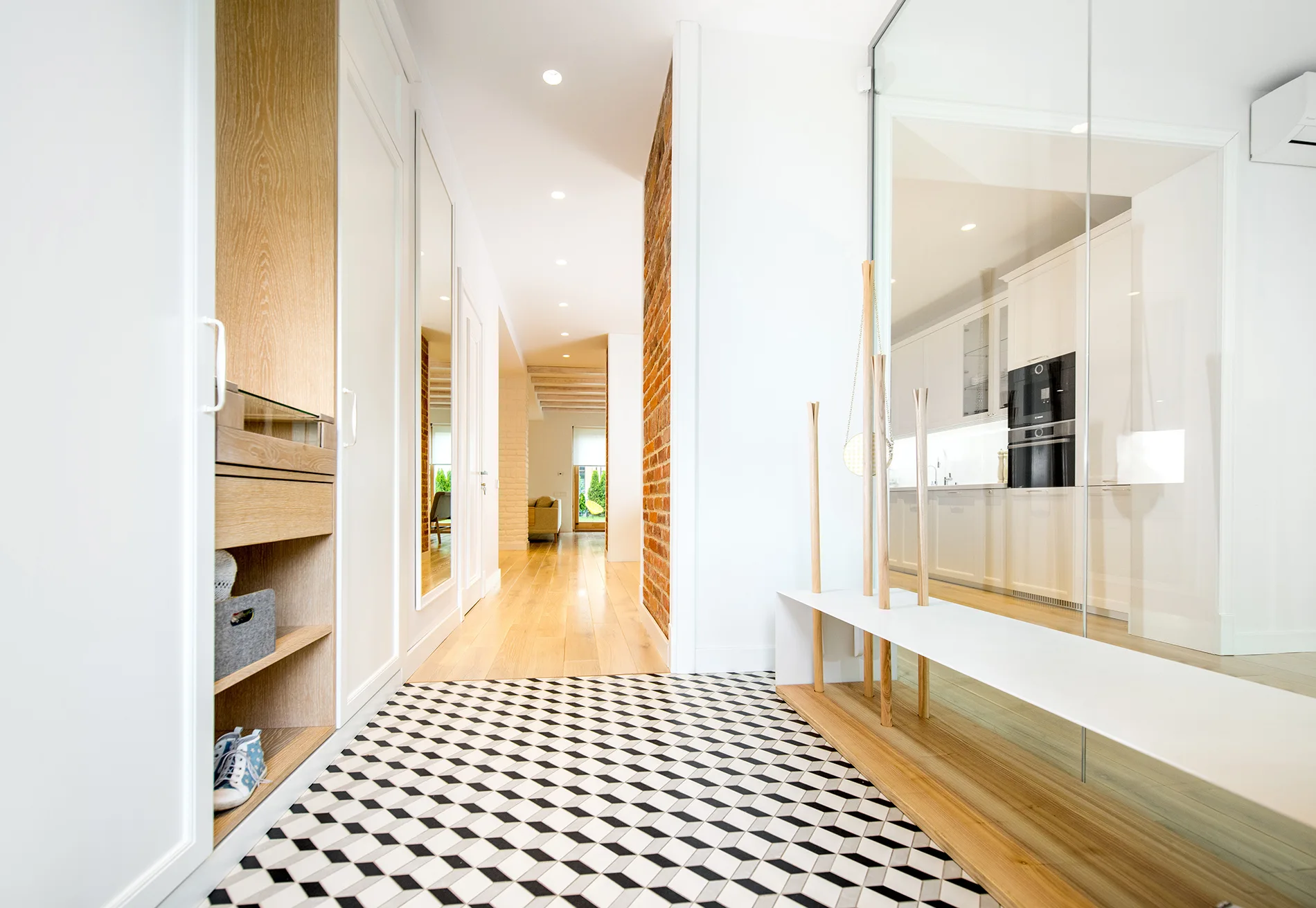 A modern home entryway features bold geometric floor tiles transitioning into wood flooring, custom built-in closets, and a glass room divider.
