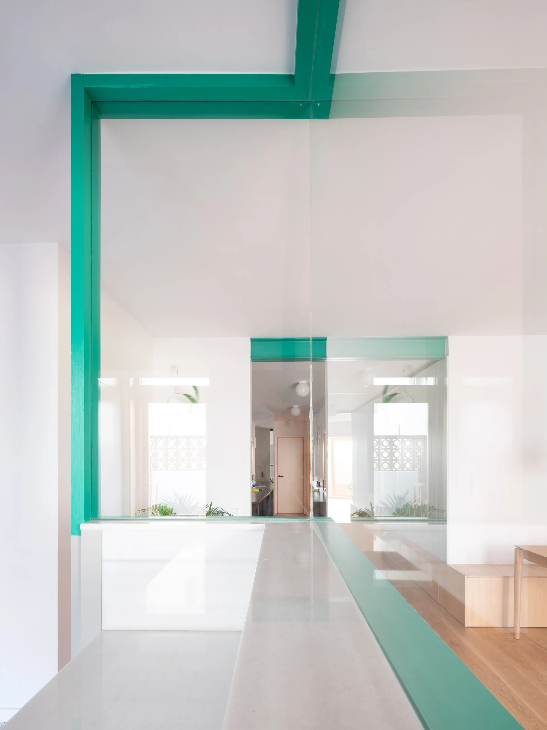 A minimalist interior hallway features a clear glass partition wall framed with bold green painted structural beams and smooth white walls.