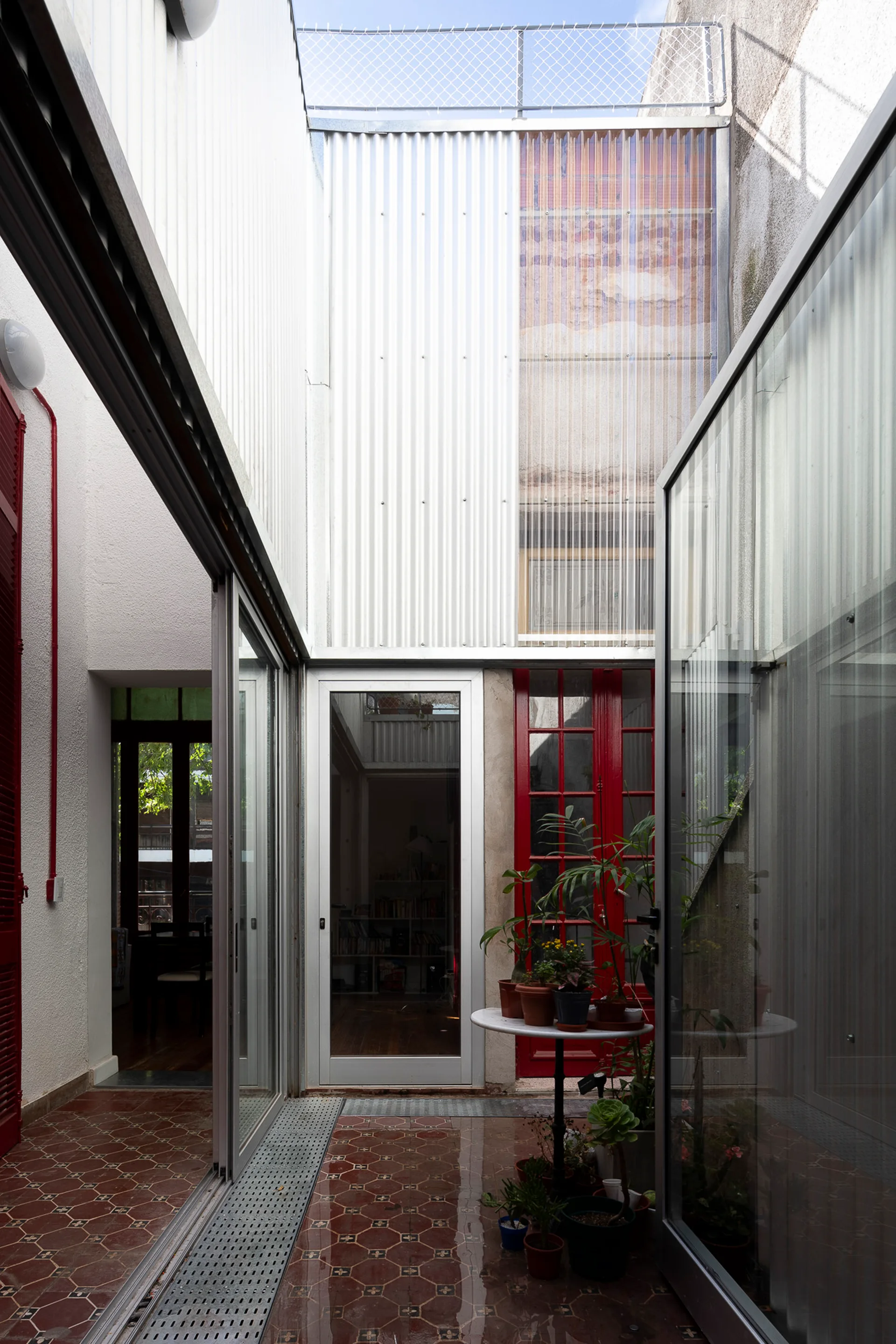 A small outdoor courtyard featuring patterned red tile flooring, corrugated metal walls, and large glass sliding doors leading to indoor rooms.