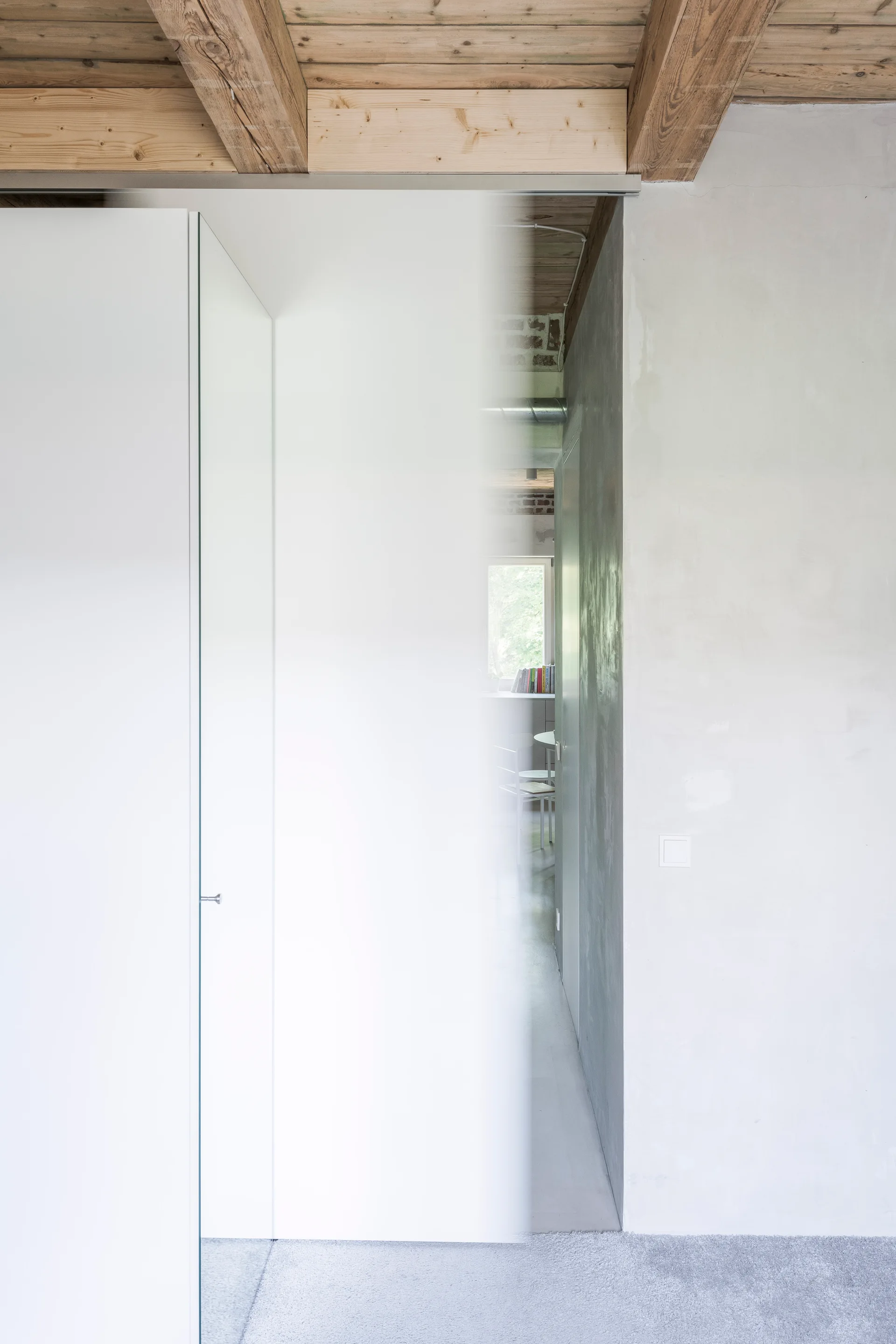 A minimalist white partition stands next to an unfinished plaster wall beneath an exposed timber beam ceiling.