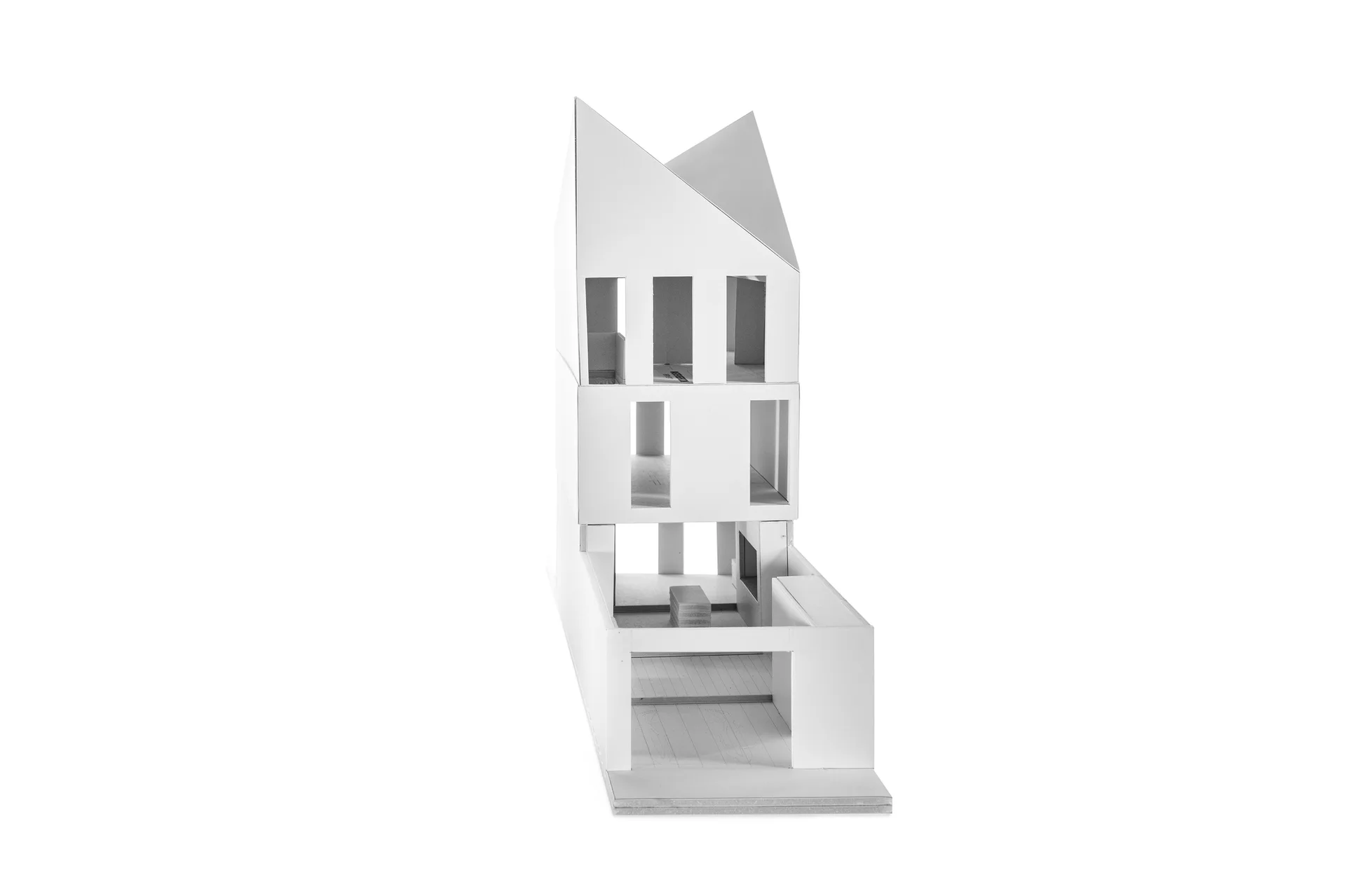 A white foam core architectural scale model of a multi-story house with a peaked roof and rectangular window cutouts, set against a plain white background.