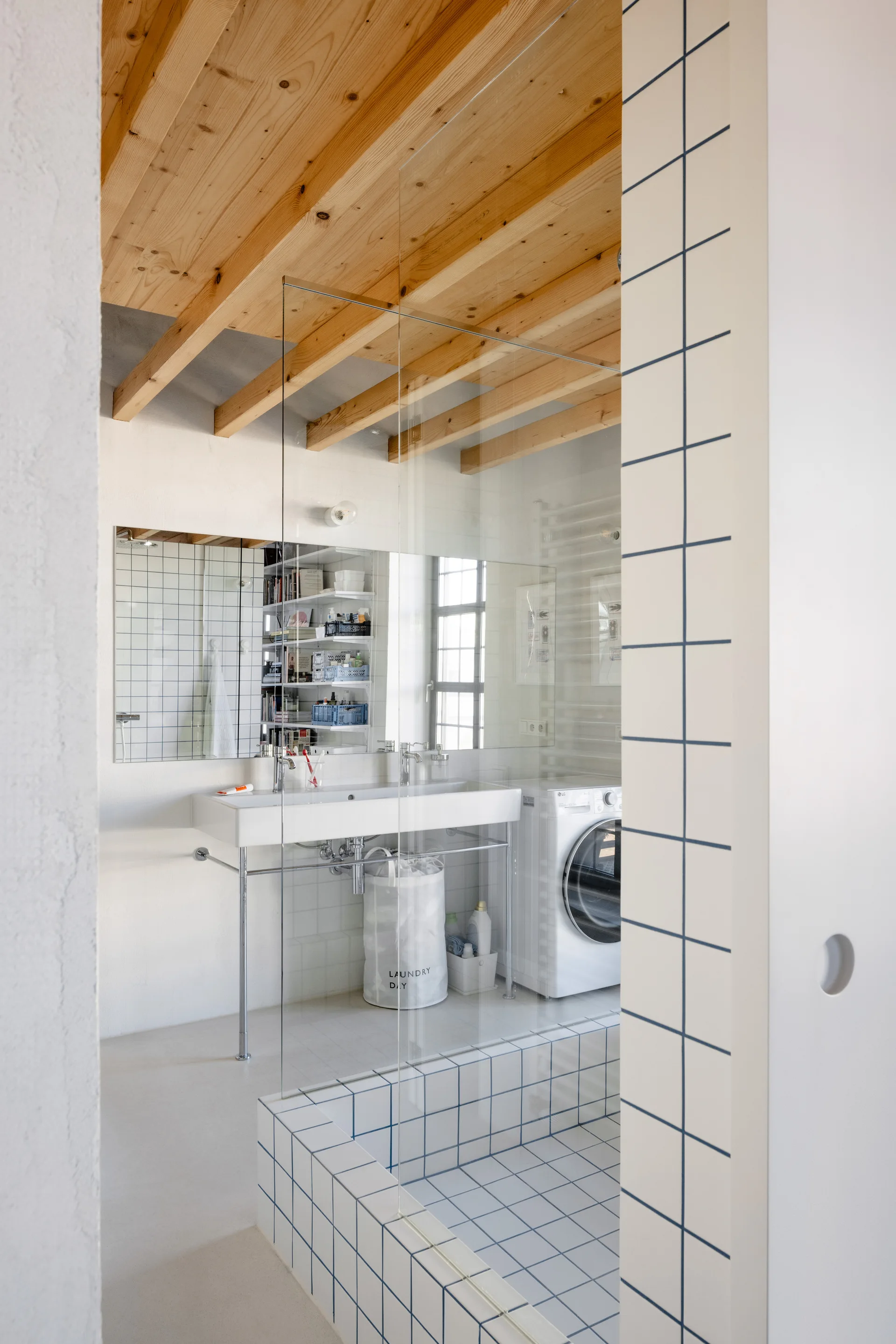 A minimalist bathroom with exposed wood ceiling beams, a console sink, and white square tiles featuring contrasting blue grout.