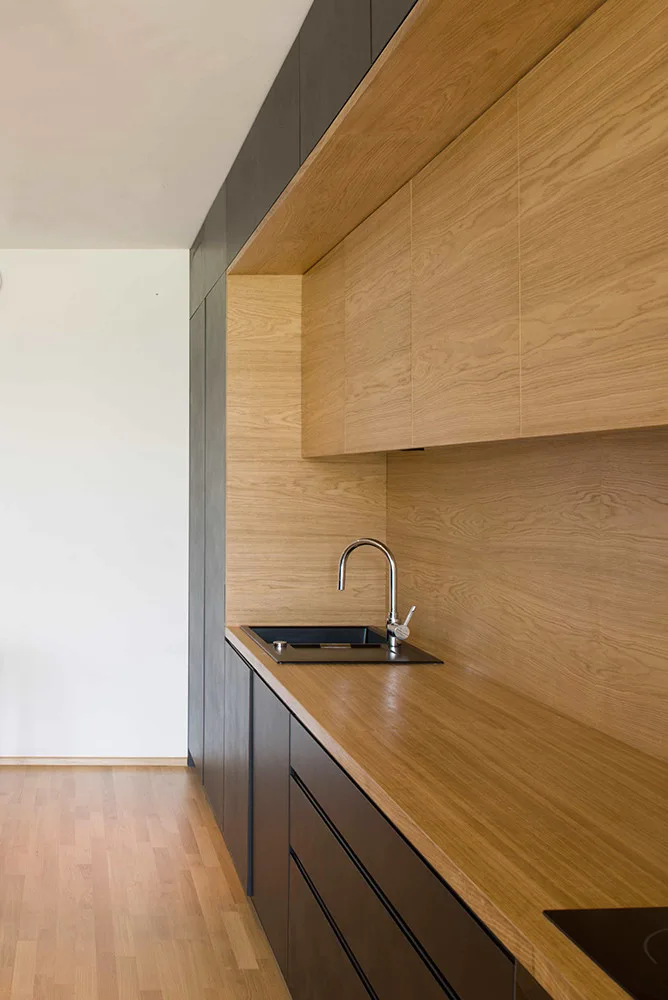 Sleek charcoal grey kitchen cabinets frame a recessed oak wood niche featuring matching countertops, upper cabinets, and a black undermount sink.