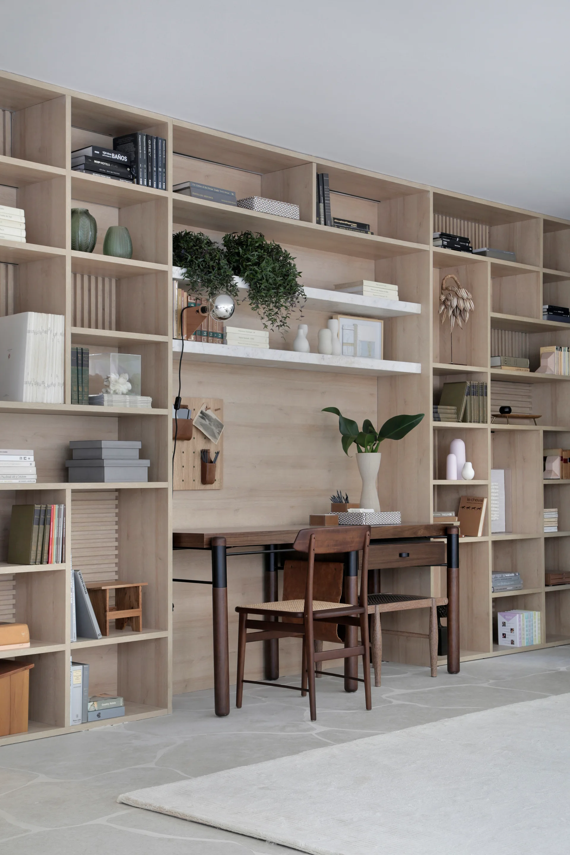 A large light wood grid shelving unit covers a wall, featuring an integrated wooden desk with a cane chair and curated decorative objects.