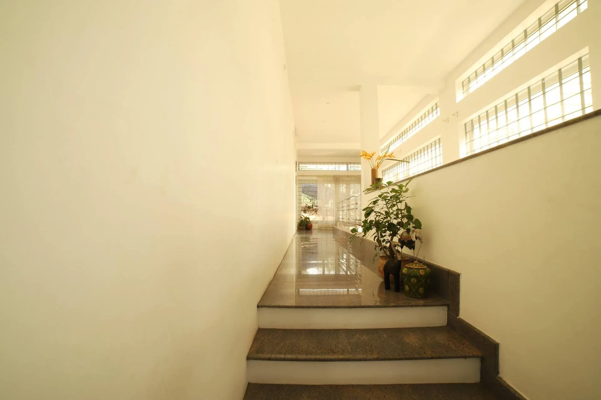 A minimalist interior staircase landing features polished grey stone steps, plain white walls, and a row of glass block windows letting in natural light.